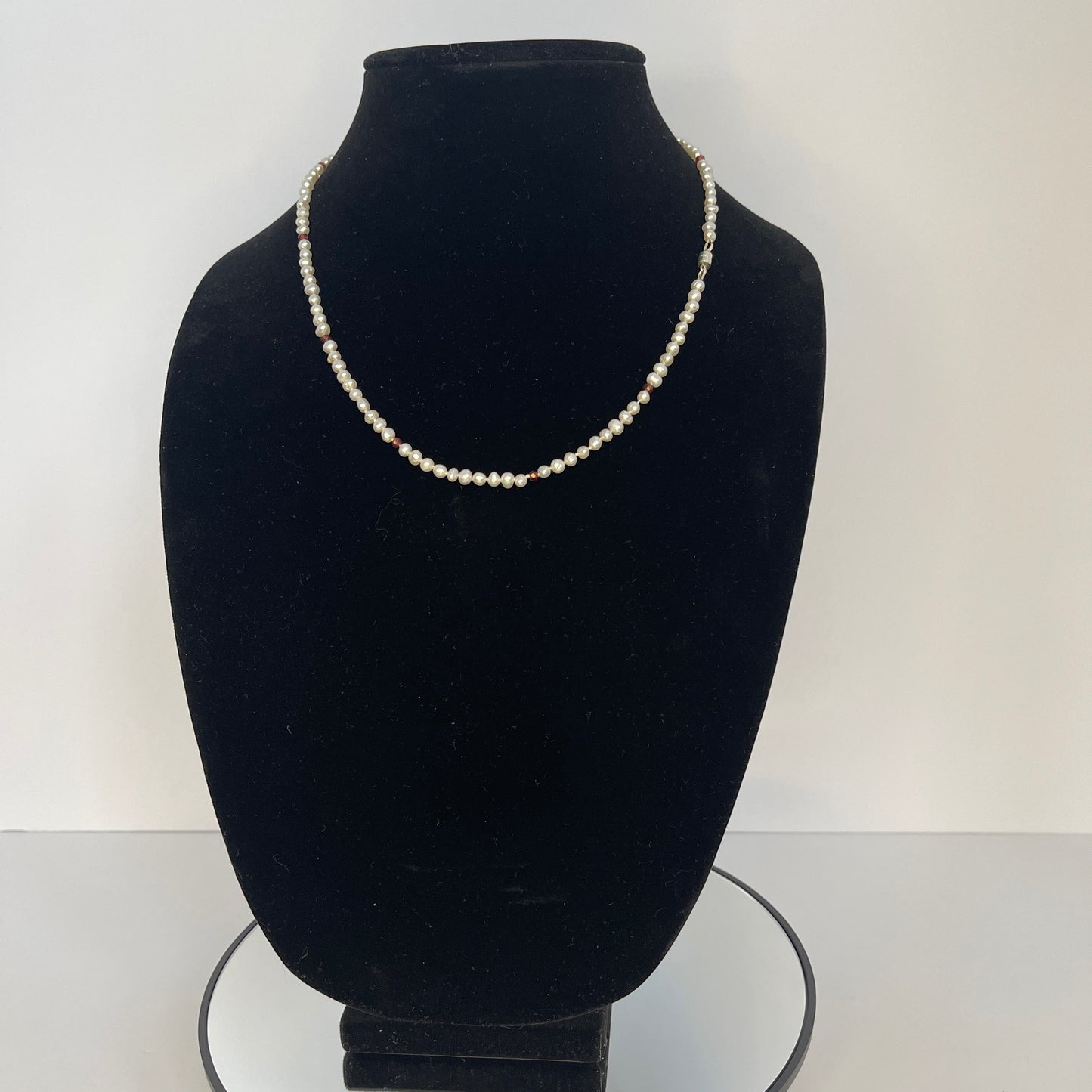 Pearl and red cubic zirconia necklace on a black mannequin bust with a white background