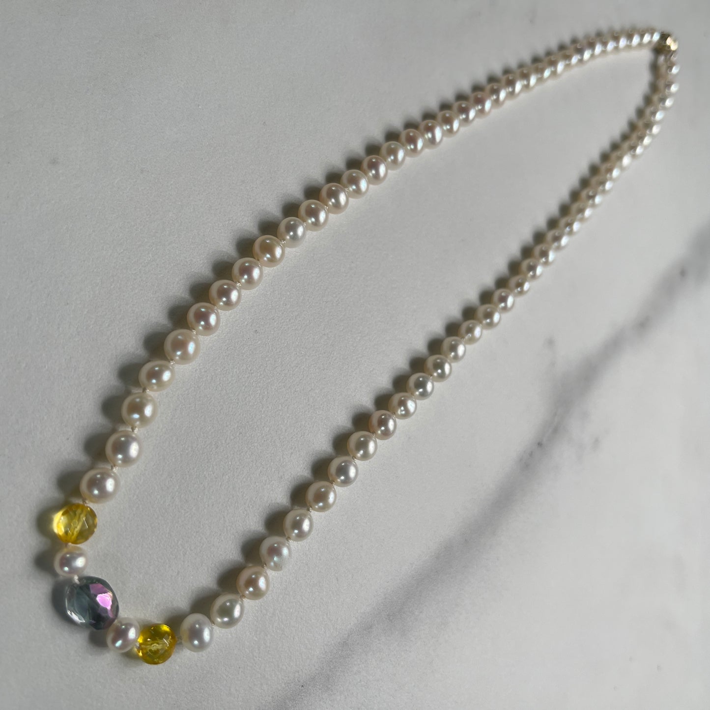 Pearl necklace with citrine and rainbow tourmaline accents on a marble surface