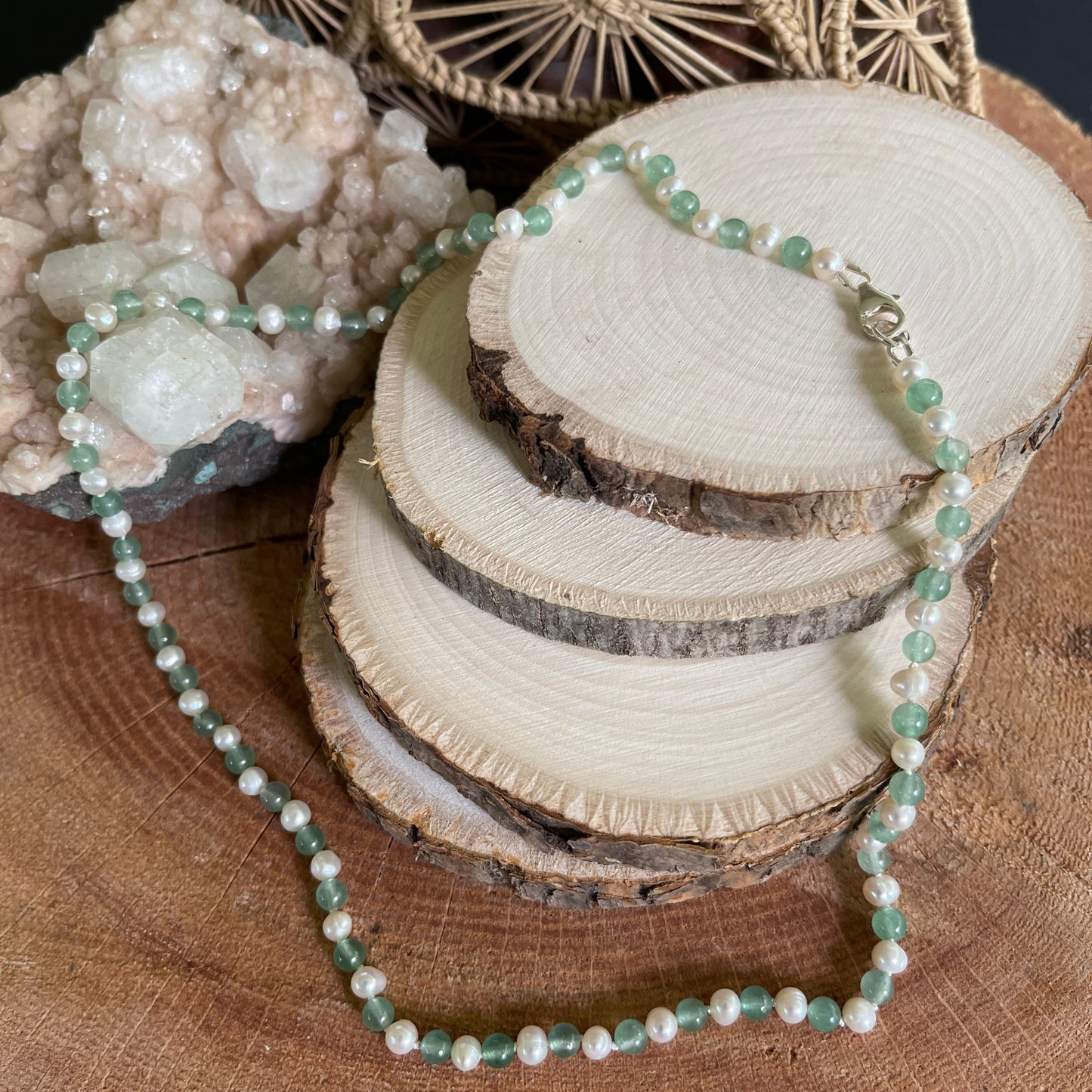 Necklace with green aventurine beads and white freshwater Pearls on a wooden surface with crystals and natural wood slices.
