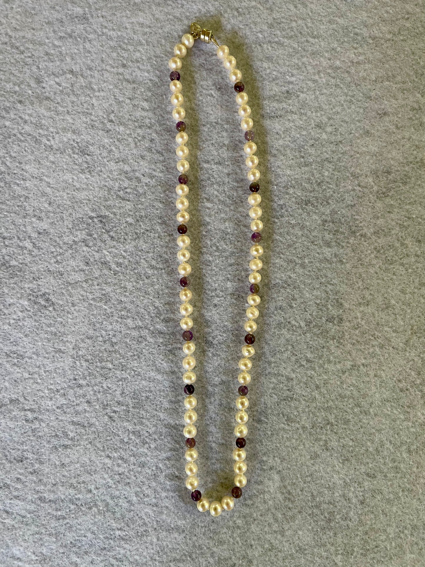 Beaded necklace with alternating white Pearls and Amethyst beads on a gray surface