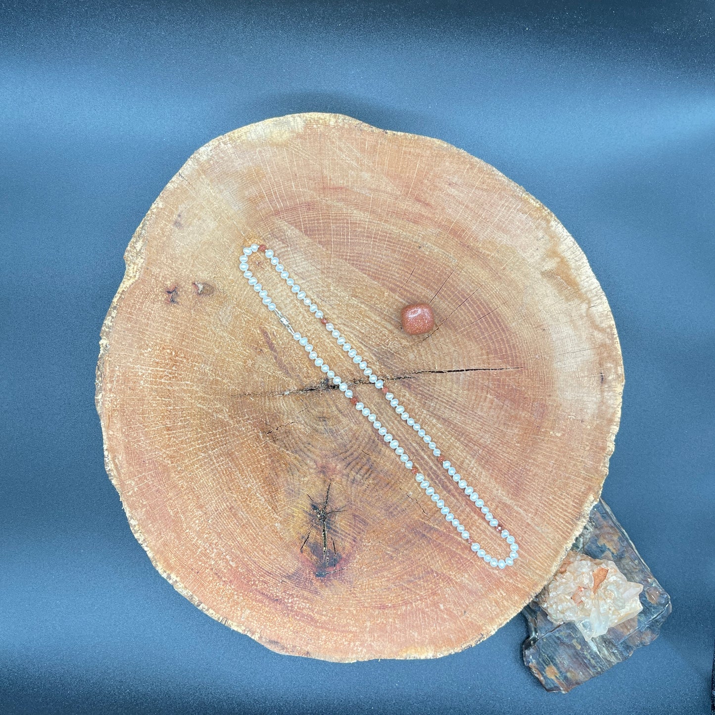 Pearl and goldstone necklace on a wooden surface with a stone