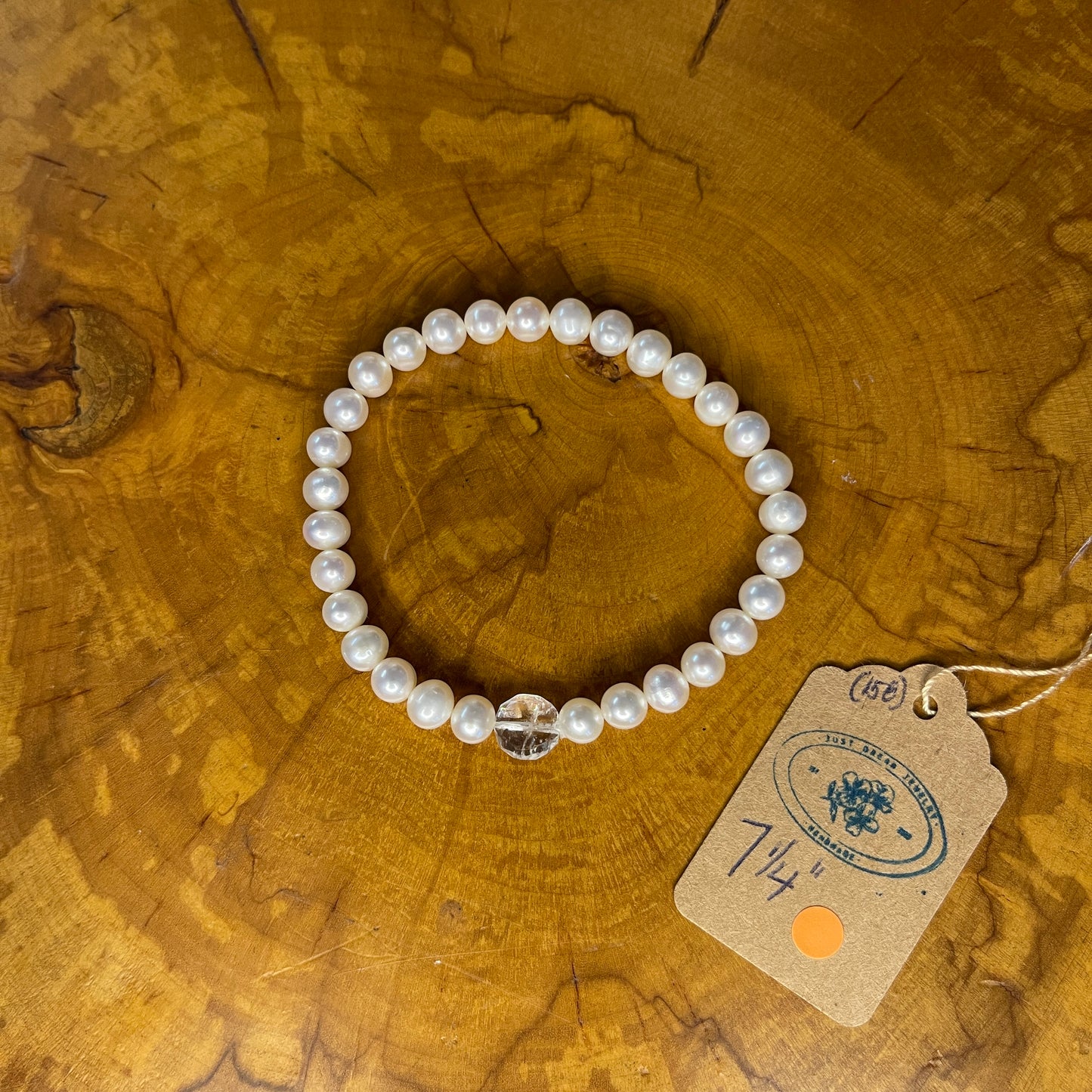 White freshwater Pearls with Quartz focus bead on elastic, 7 1/4" on wooden surface with tag