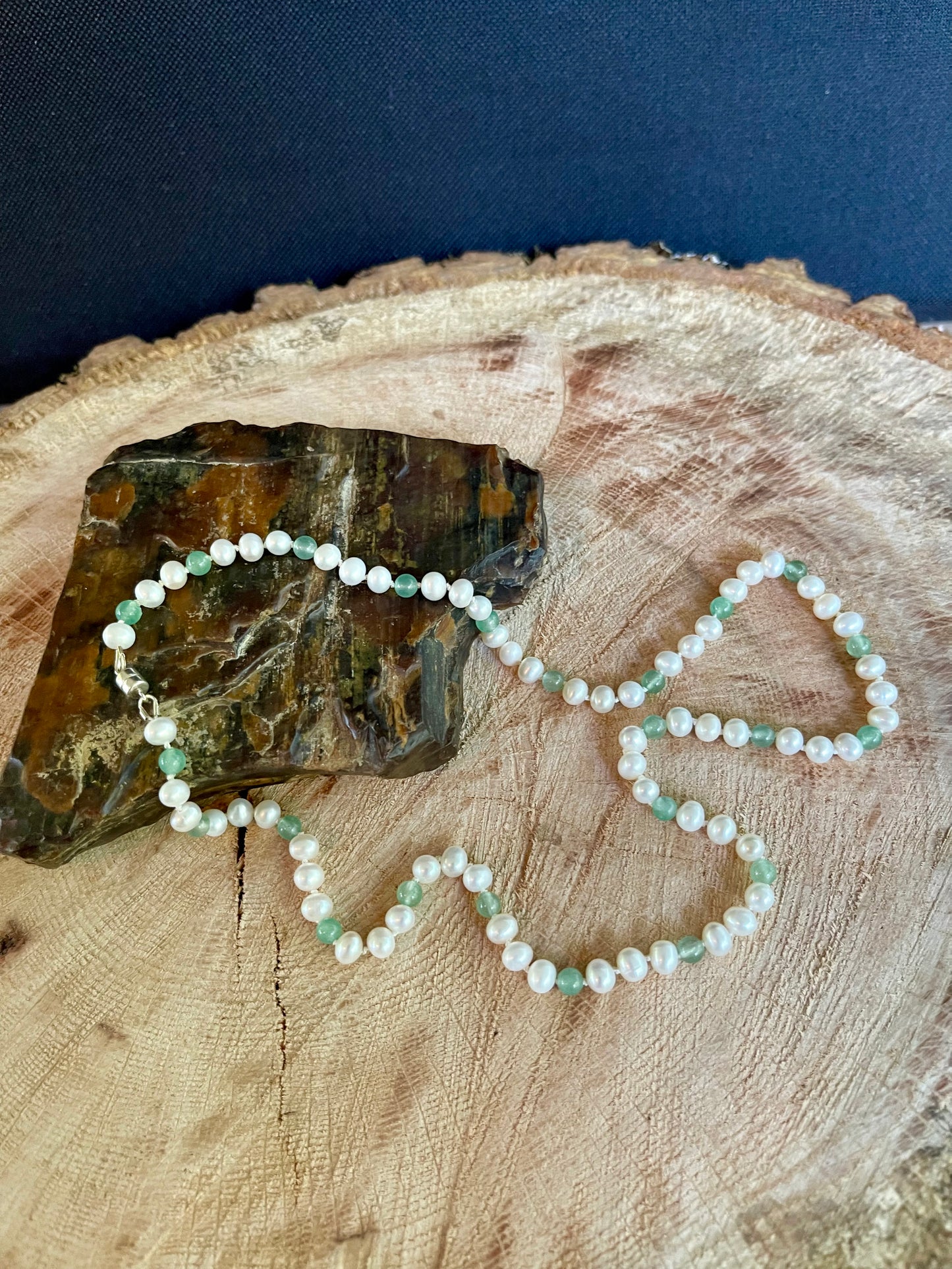 Pearl and Aventurine bead necklace draped over a piece of petrified wood on a wooden surface with a dark background