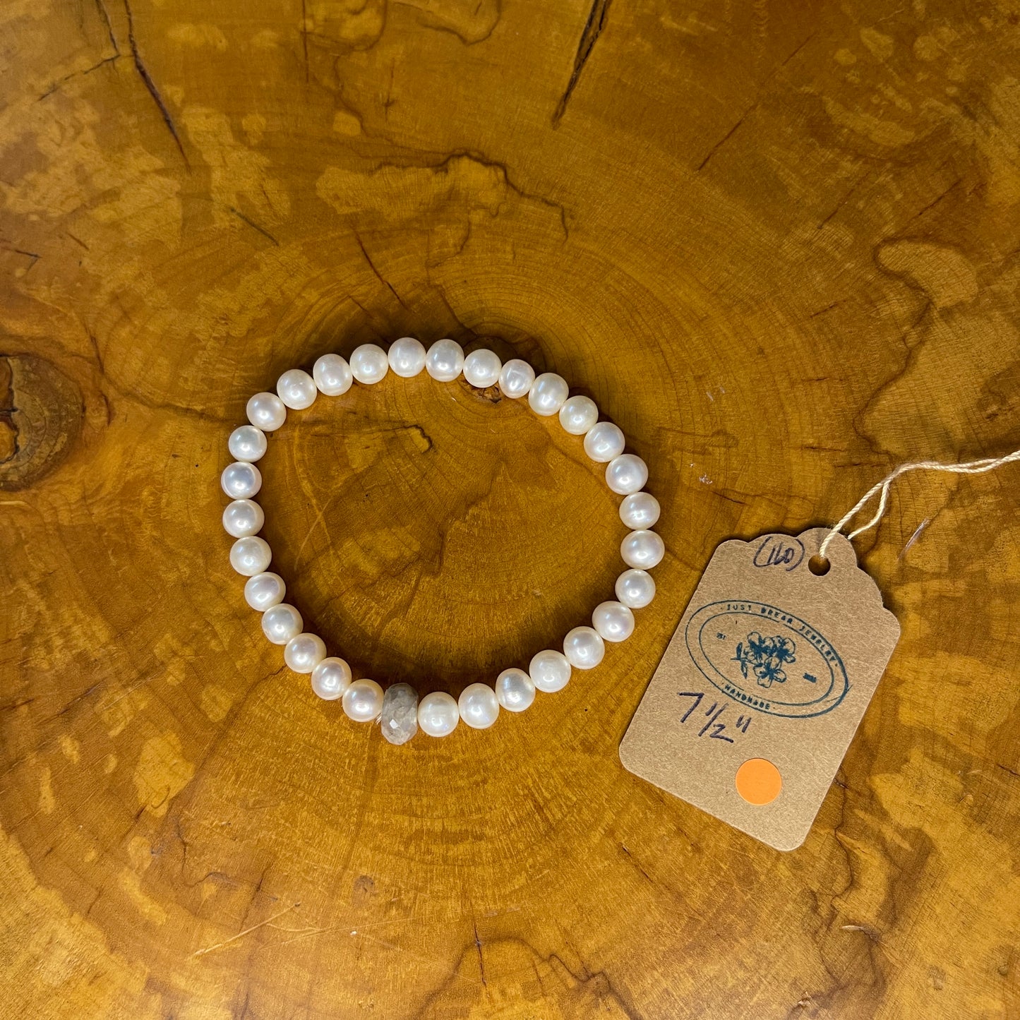 White freshwater Pearls with Grey Chalcedony Rondelle focus bead on elastic, 7 1/2" on a wooden surface with tag