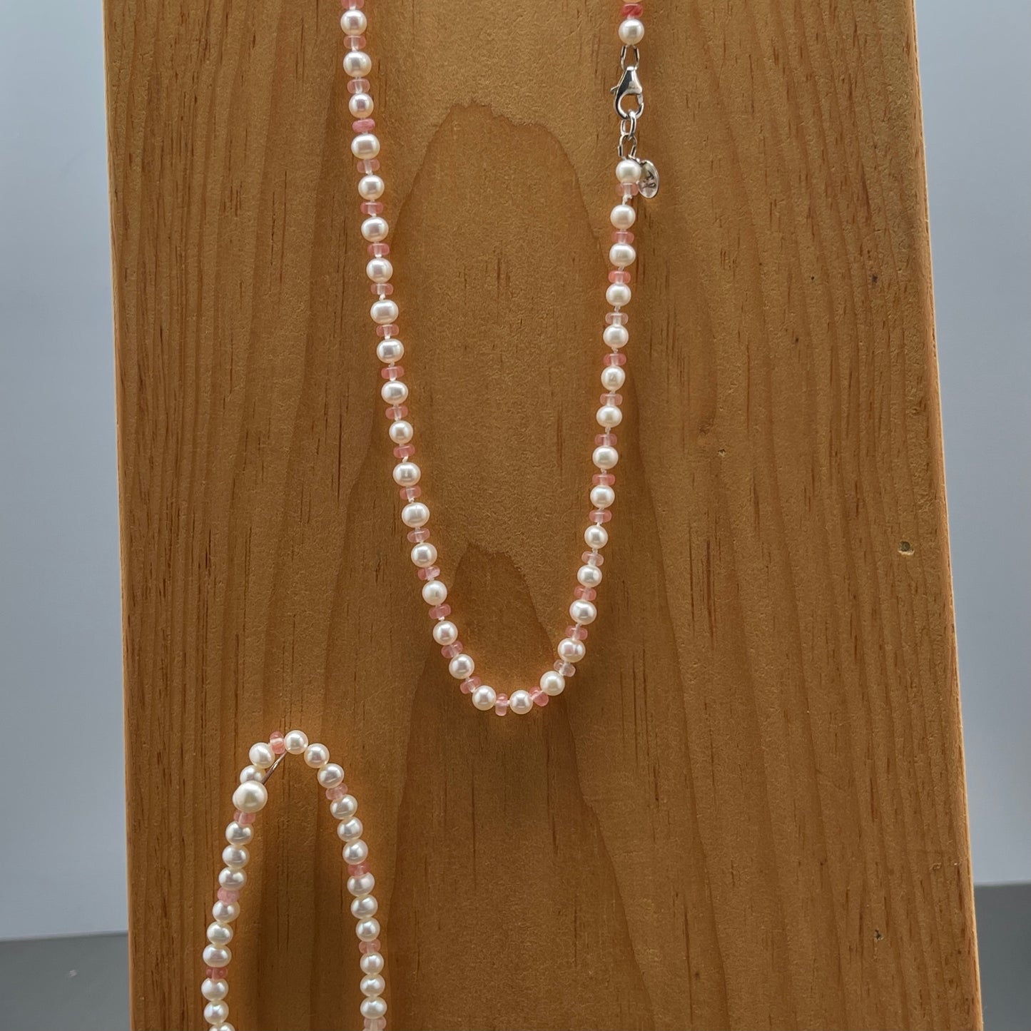 White Pearl and strawberry quartz necklace and matching stretchy bracelet on a wooden surface
