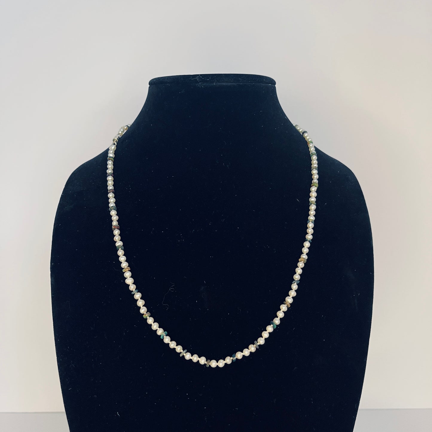 Pearl and Black Opal necklace on a black velvet stand against a white background
