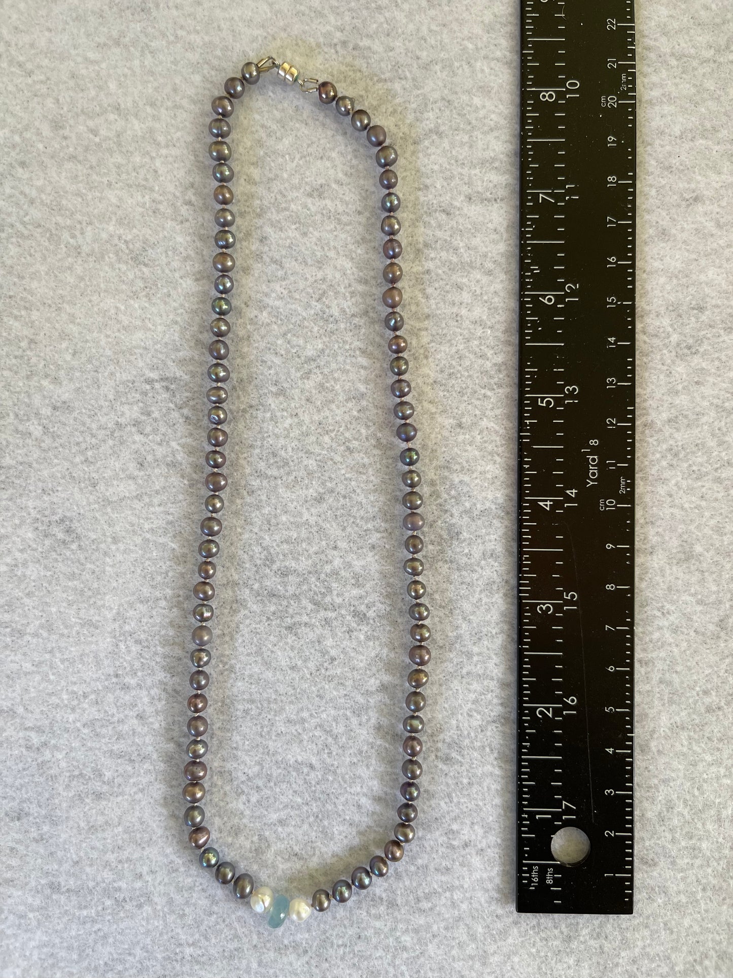 Necklace of Silver Peacock pearls with Aquamarine and Rainbow Tourmaline focus beads on a white surface with ruler