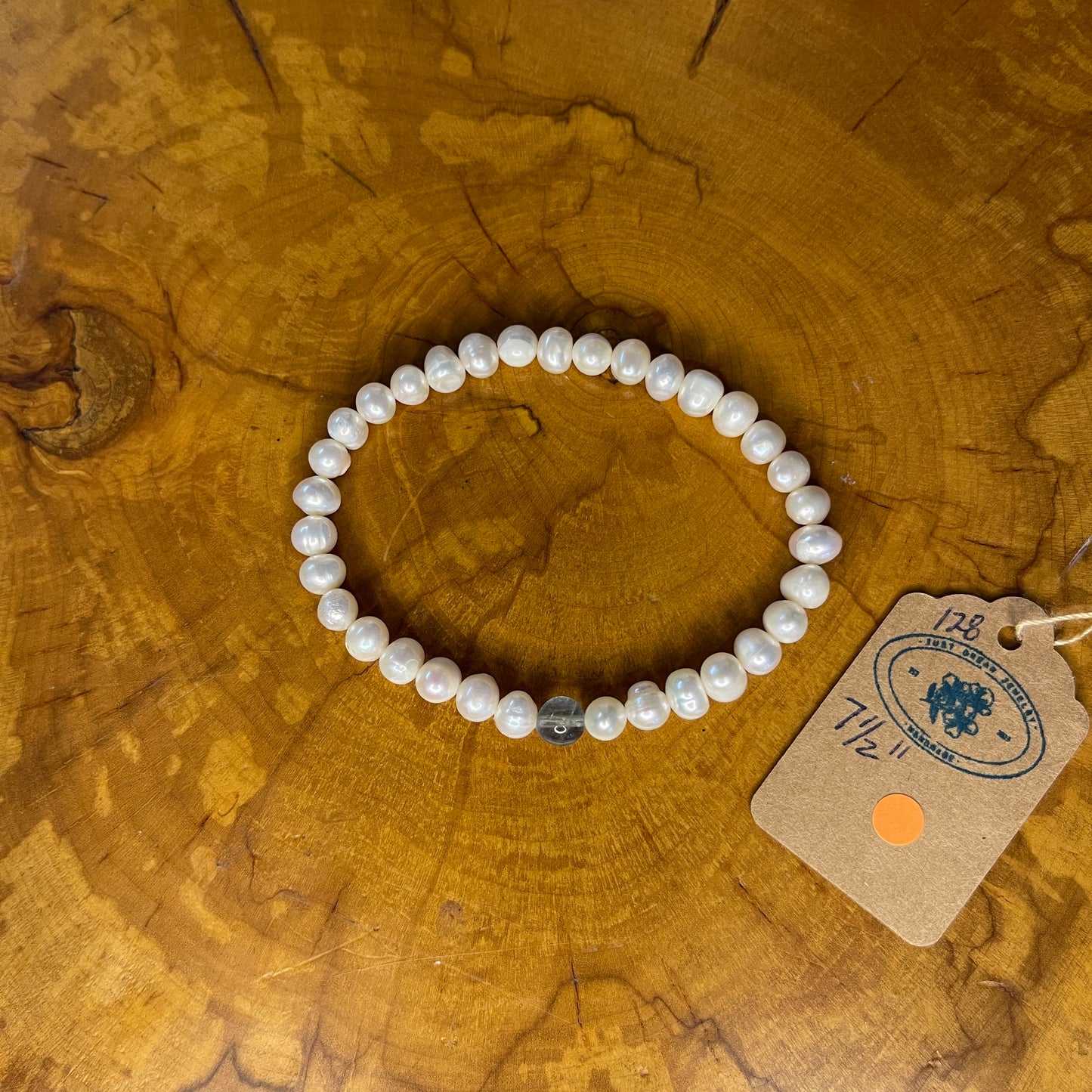 Freshwater White Pearls with Fluorite focus bead on elastic, 7 1/2" on wooden surface with tag