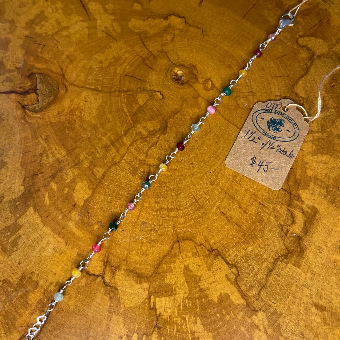 Multi colored faceted jade on Sterling Silver wire, 7 1/2 "with 1/2" Sterling heart chain extender on a wooden surface with tag