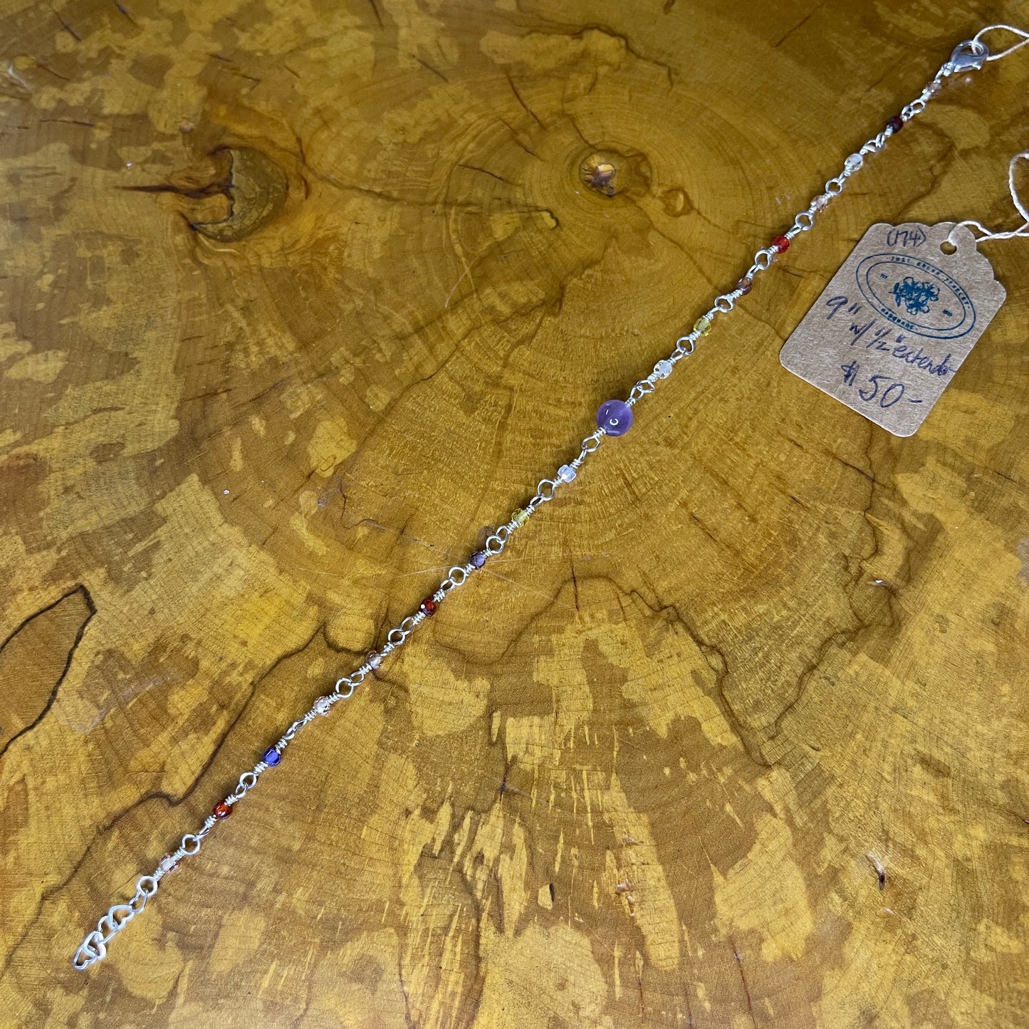 Multi colored Cubic Zirconia with Amethyst focus bead on Sterling Silver wire with Sterling Silver 1/2" heart chain extender, 9" on wooden slab