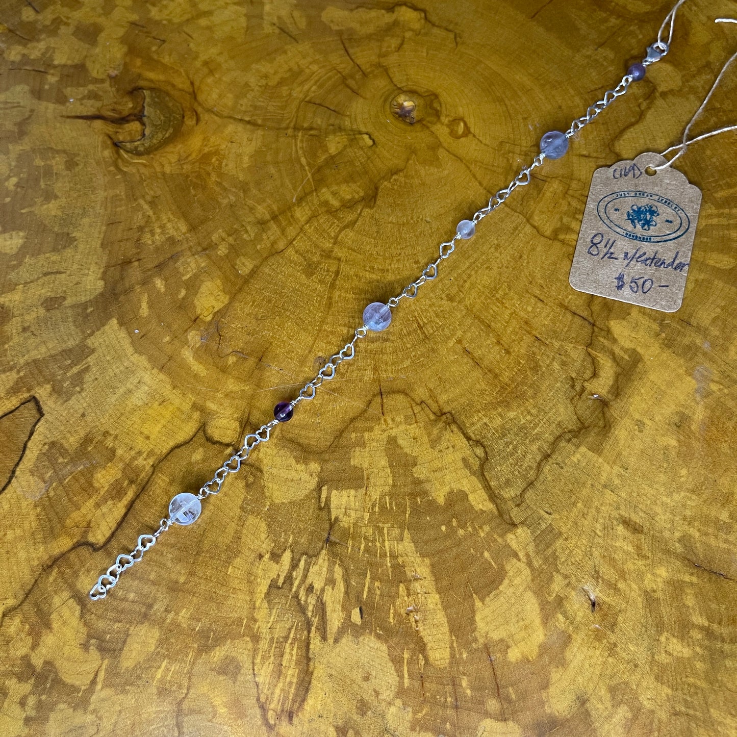 Fluorite on Sterling Silver Wire, 9" with 1/2 " Sterling Silver Heart Chain Extender on a wooden surface with tag