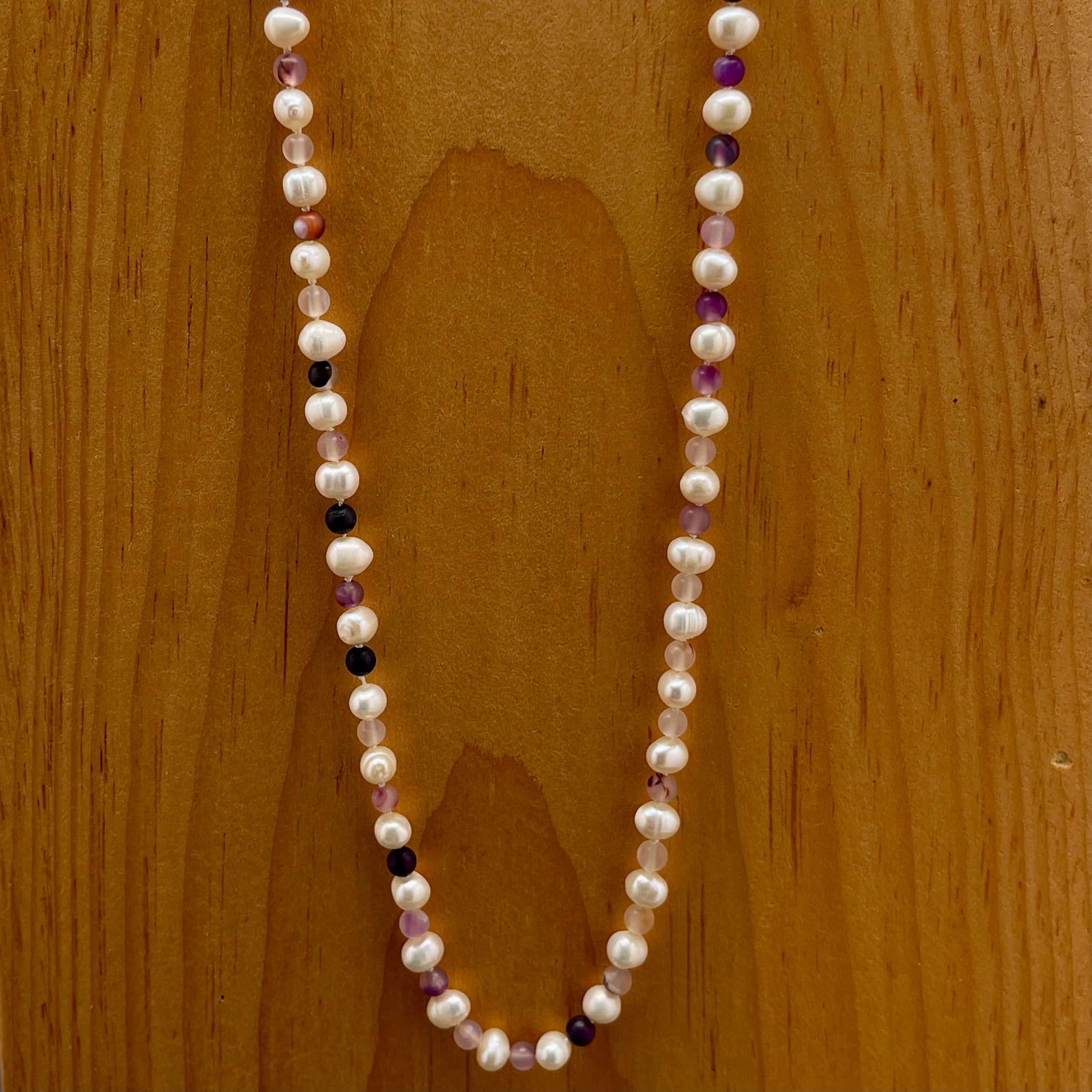 Pearl necklace with purple jasper beads on a wooden surface