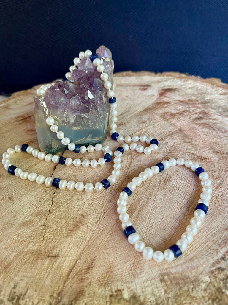 White Pearl and Lapis Lazuli heishi beaded  necklace matching stretchy bracelet on a wooden surface with a crystal background