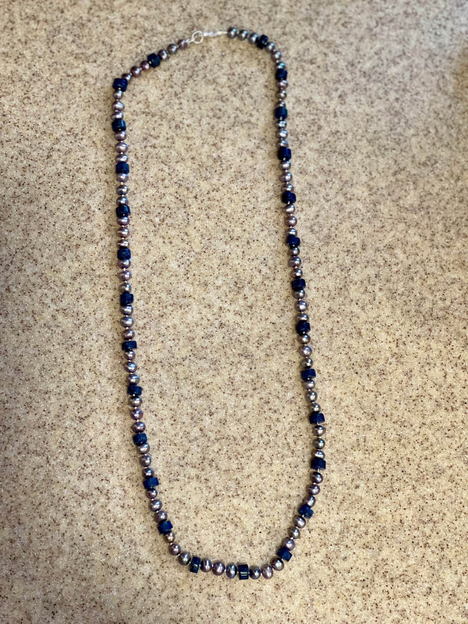 6mm silver freshwater pearls dance alongside rich lapis lazuli heishi discs necklace on pebbled sand surface