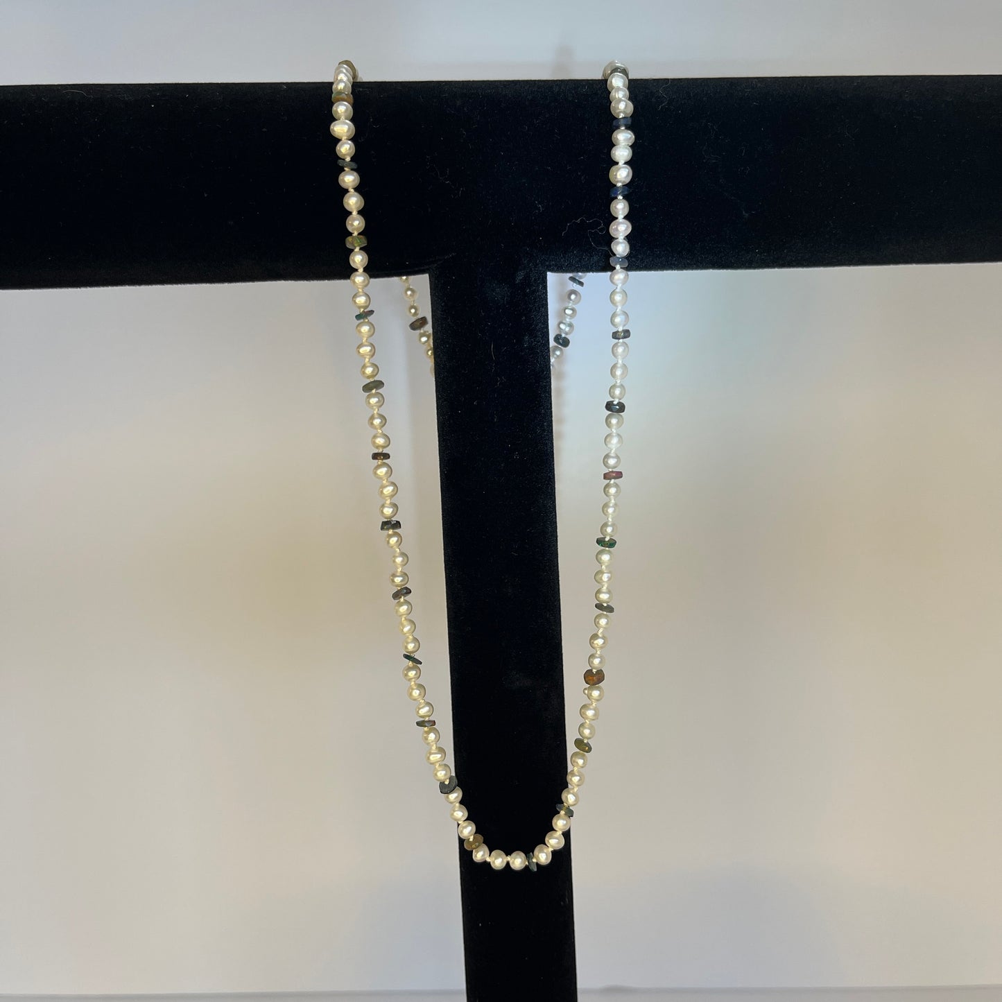 Pearl  and Black opal necklace on a black stand against a white background