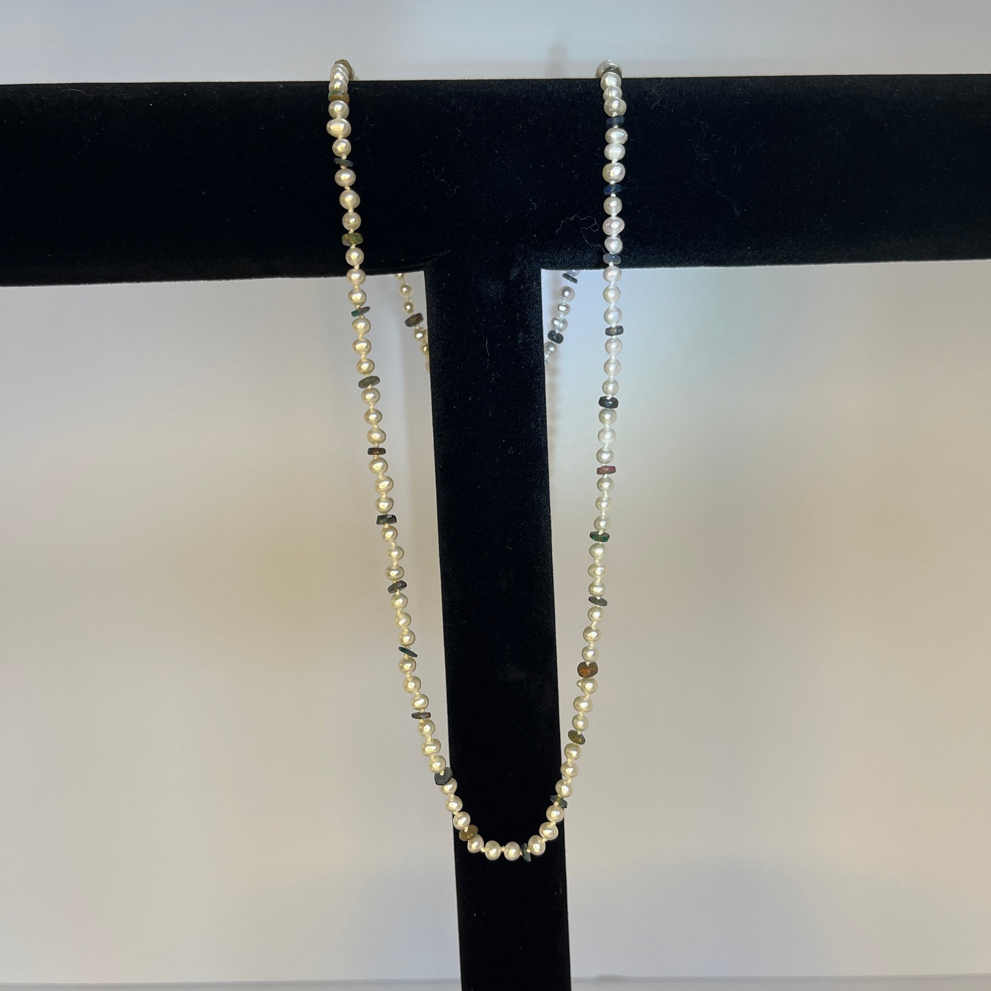 Pearl  and Black opal necklace on a black stand against a white background