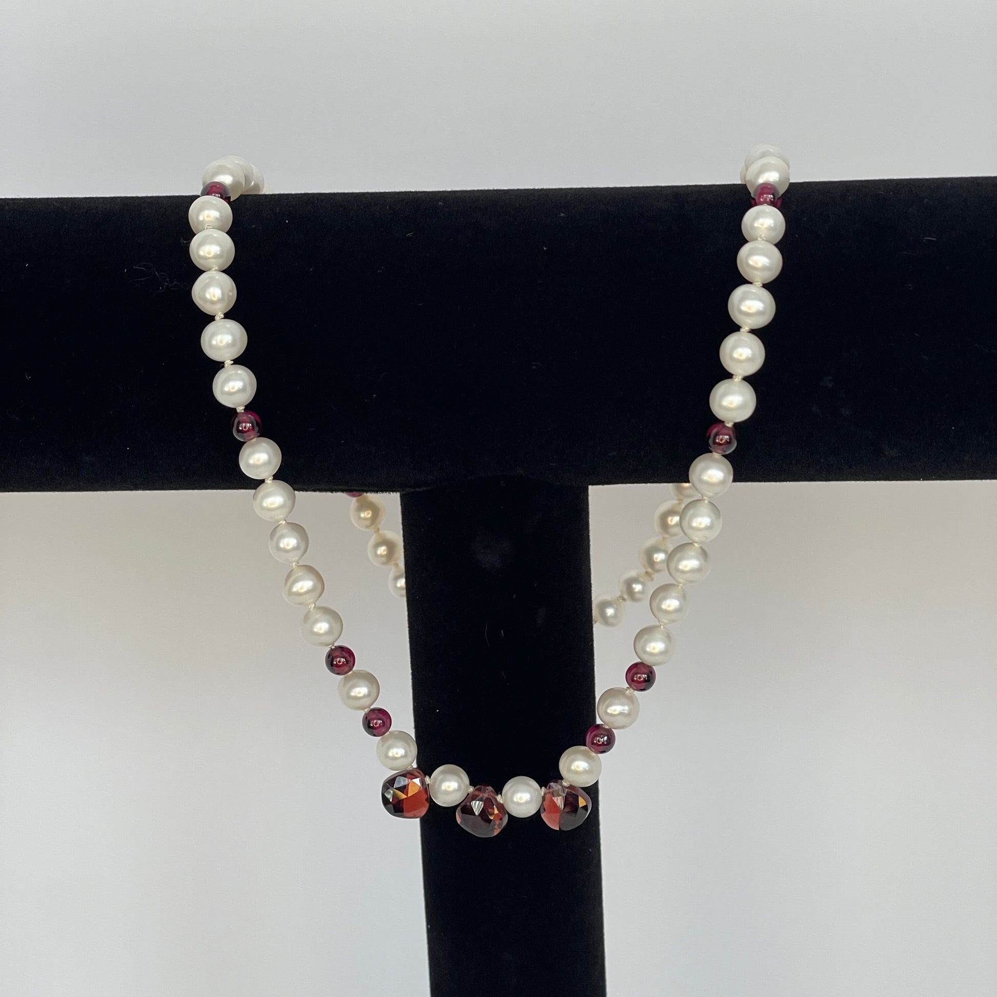 Necklace of White pearls and Garnet beads  and teardrops on a black stand against a white background