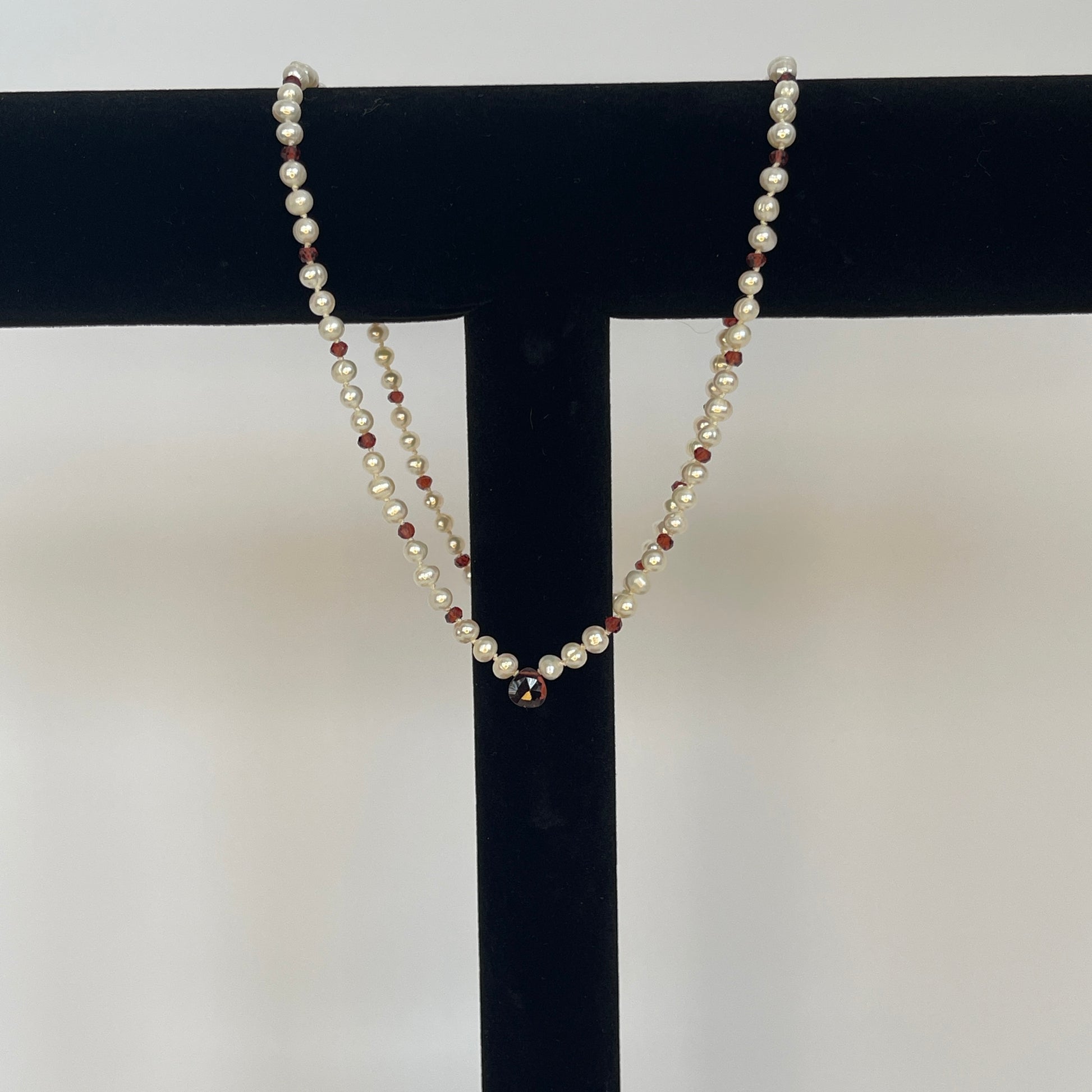 Necklace of White pearls and Garnet beads  and one teardrop on a black stand against a white background