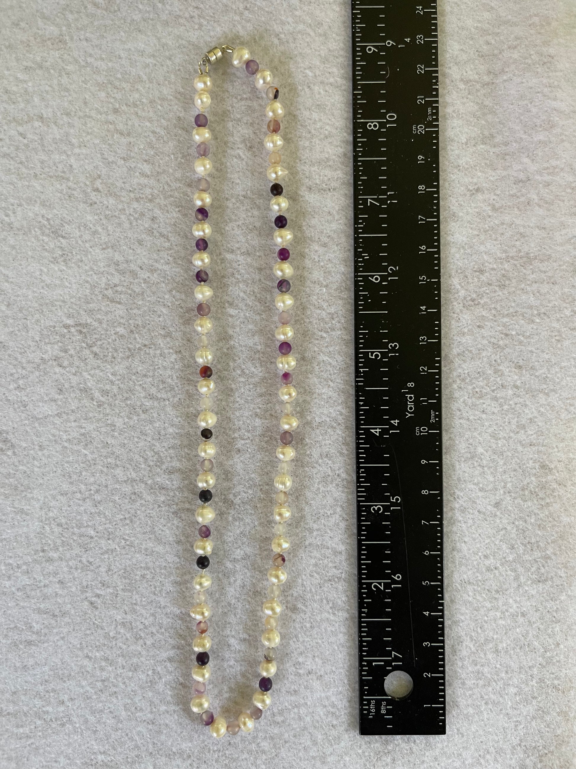 Necklace with  white Pearls and multicolored  purple jasper beads next to a ruler on a gray background