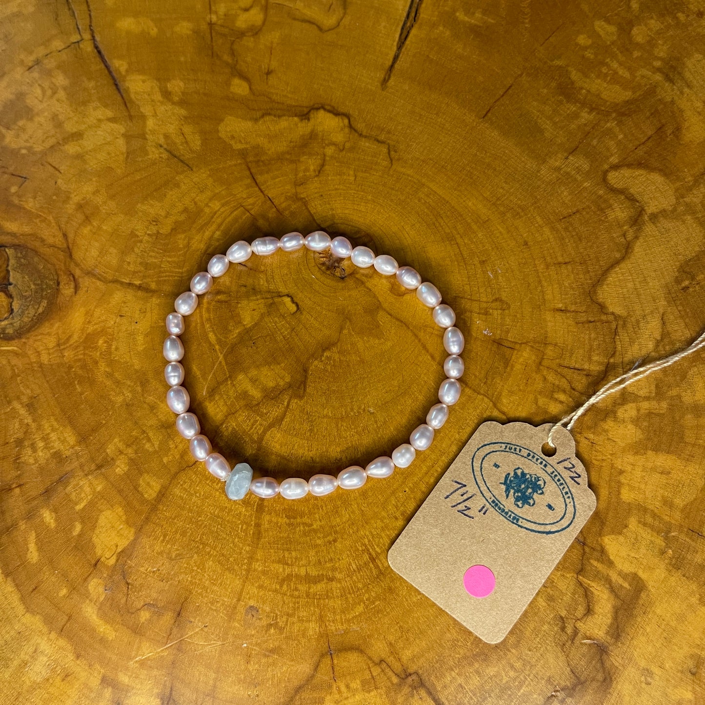 Mauve freshwater Pearls with Blue Chalcedony focus bead on elastic, 7 1/2" on elastic, 7 1/2" on a wooden surface with tag