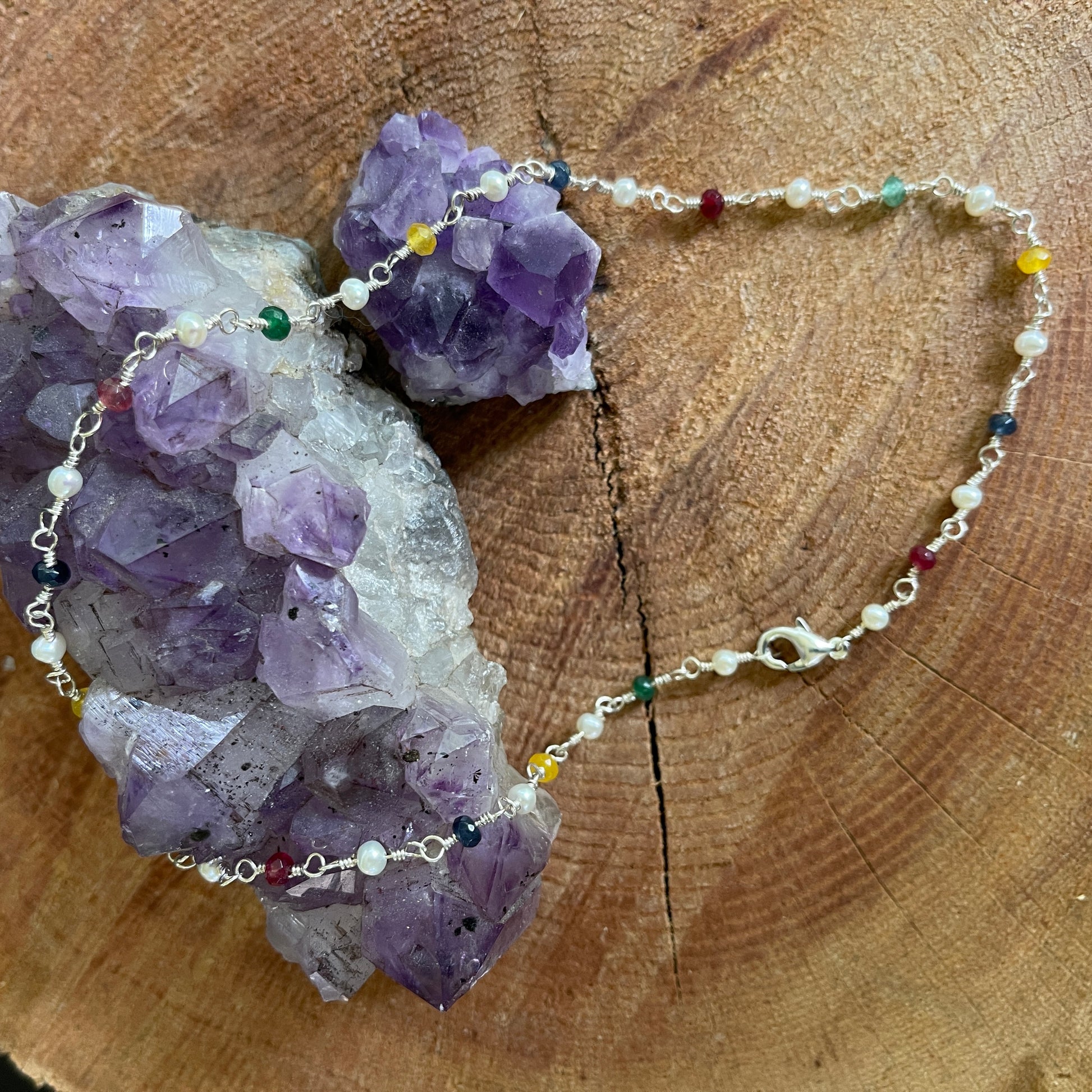 Necklace with multi colored Jade and White Pearl hand tooled on Sterling Silver wire on a wooden surface