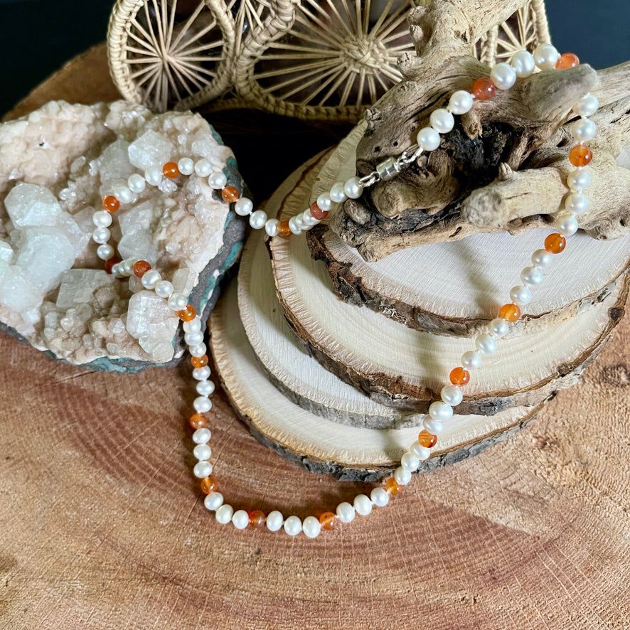 Necklace with white pearls and orange carnelian beads on a wooden surface with natural elements