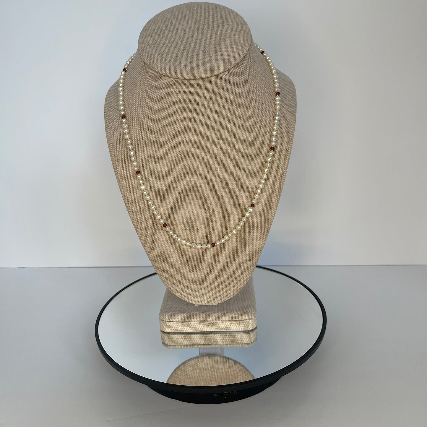 Pearl  and red cubic zirconia necklace on a beige mannequin bust with a white background
