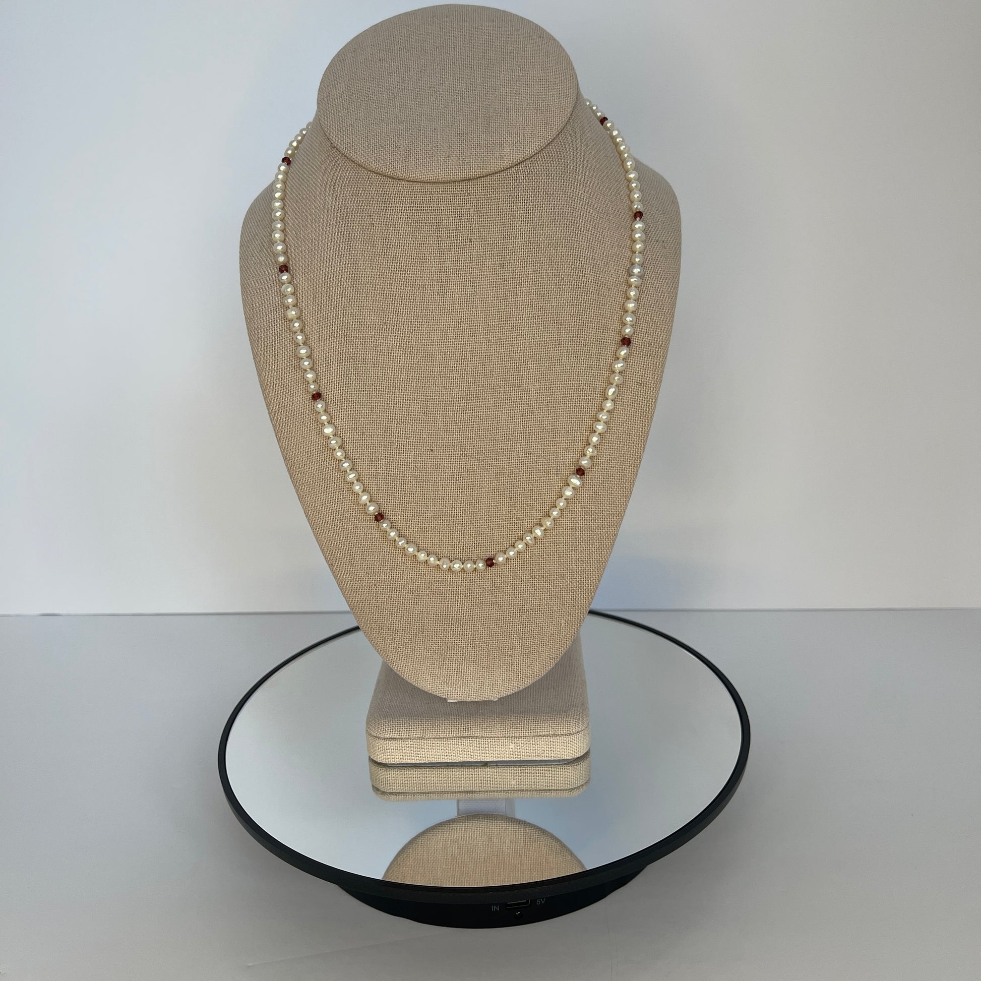 Pearl  and red cubic zirconia necklace on a beige mannequin bust with a white background