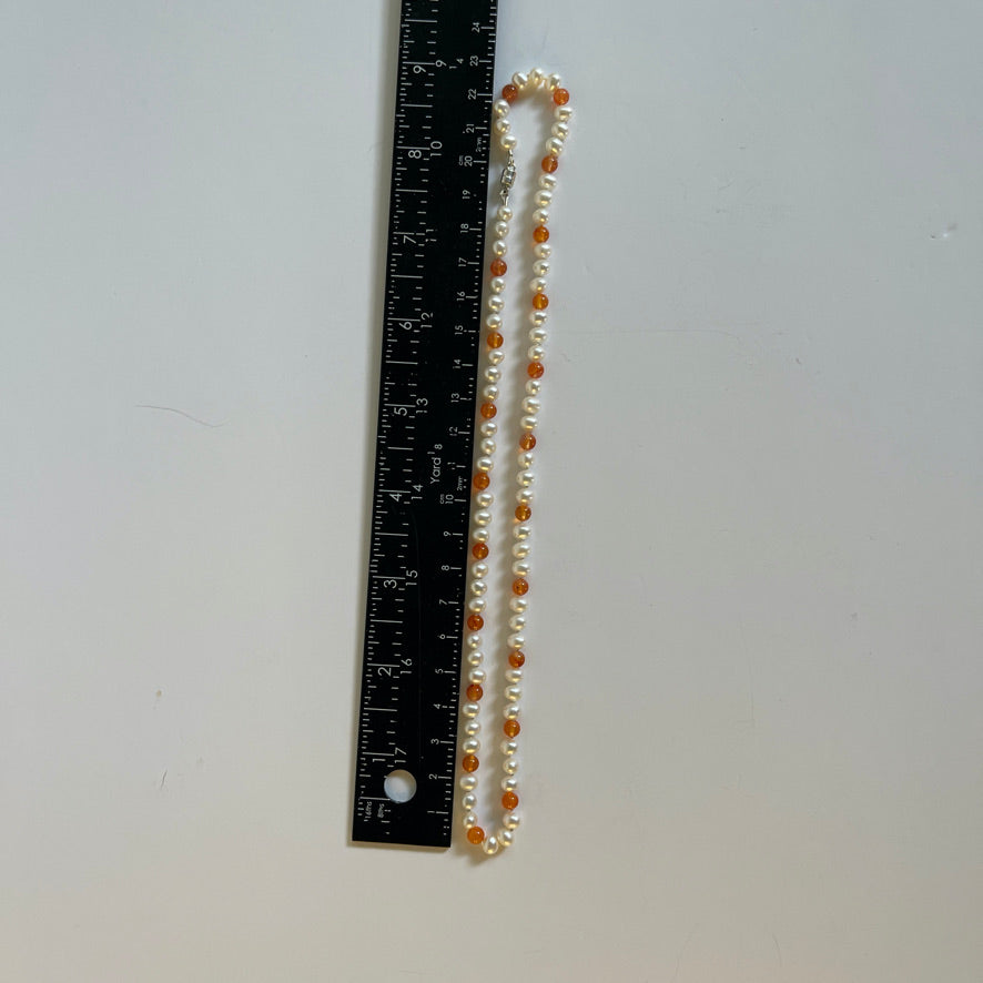 Necklace with white pearls and orange carnelian beads on a white background with ruler