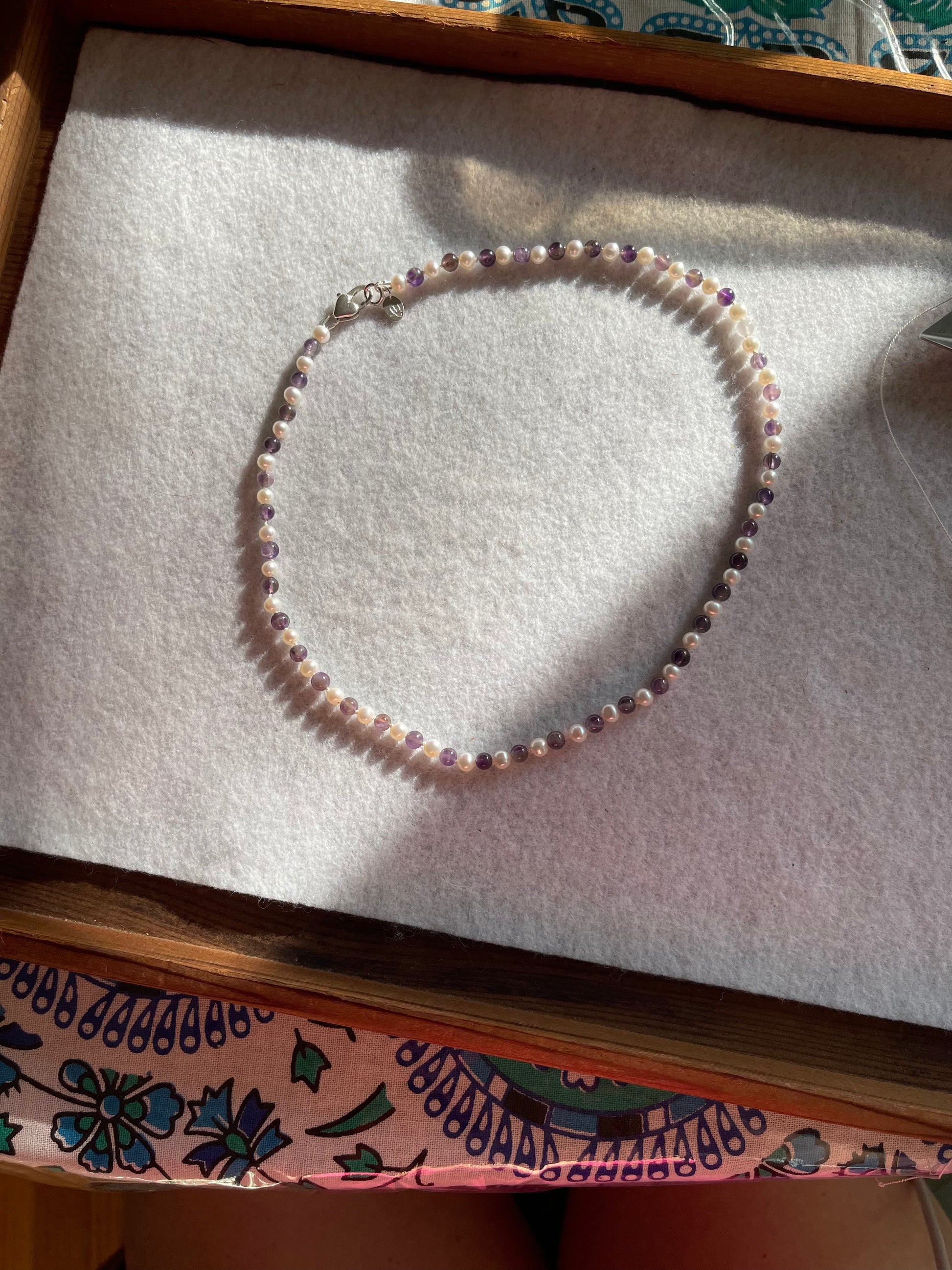 White Pearl and Amethyst Necklace on a textured surface with a decorative box in the background