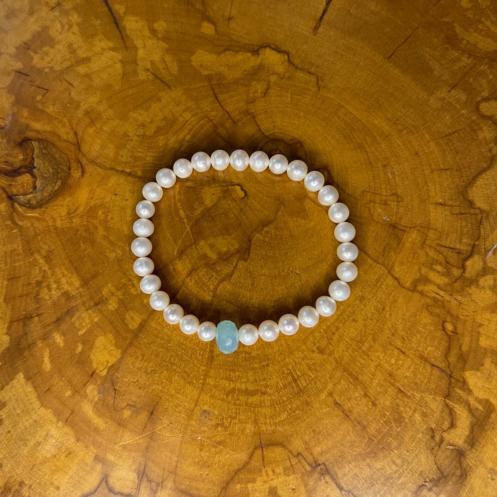 White freshwater Pearls with Aquamarine Rondelle focus bead on elastic, 7 1/2" on wooden surface