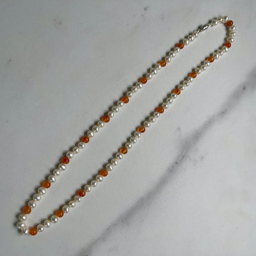 Necklace with white pearls and orange carnelian beads on a white surface with natural elements
