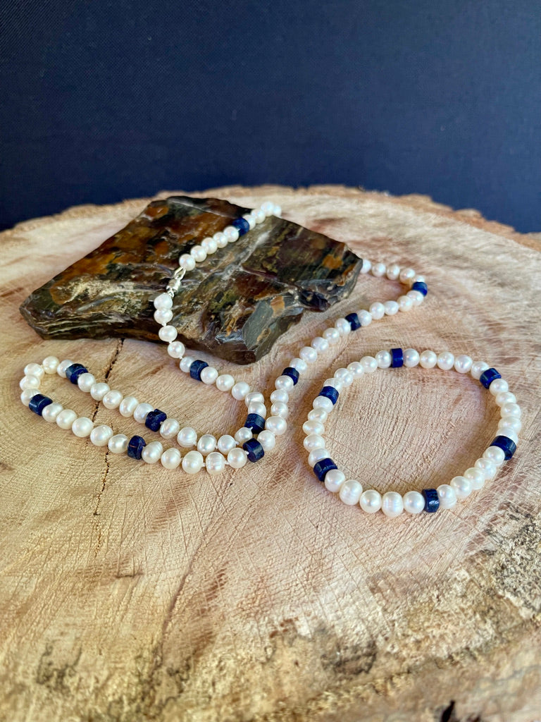 White Pearl and Lapis Lazuli heishi beaded  necklace matching stretchy bracelet on a wooden surface with a crystal background