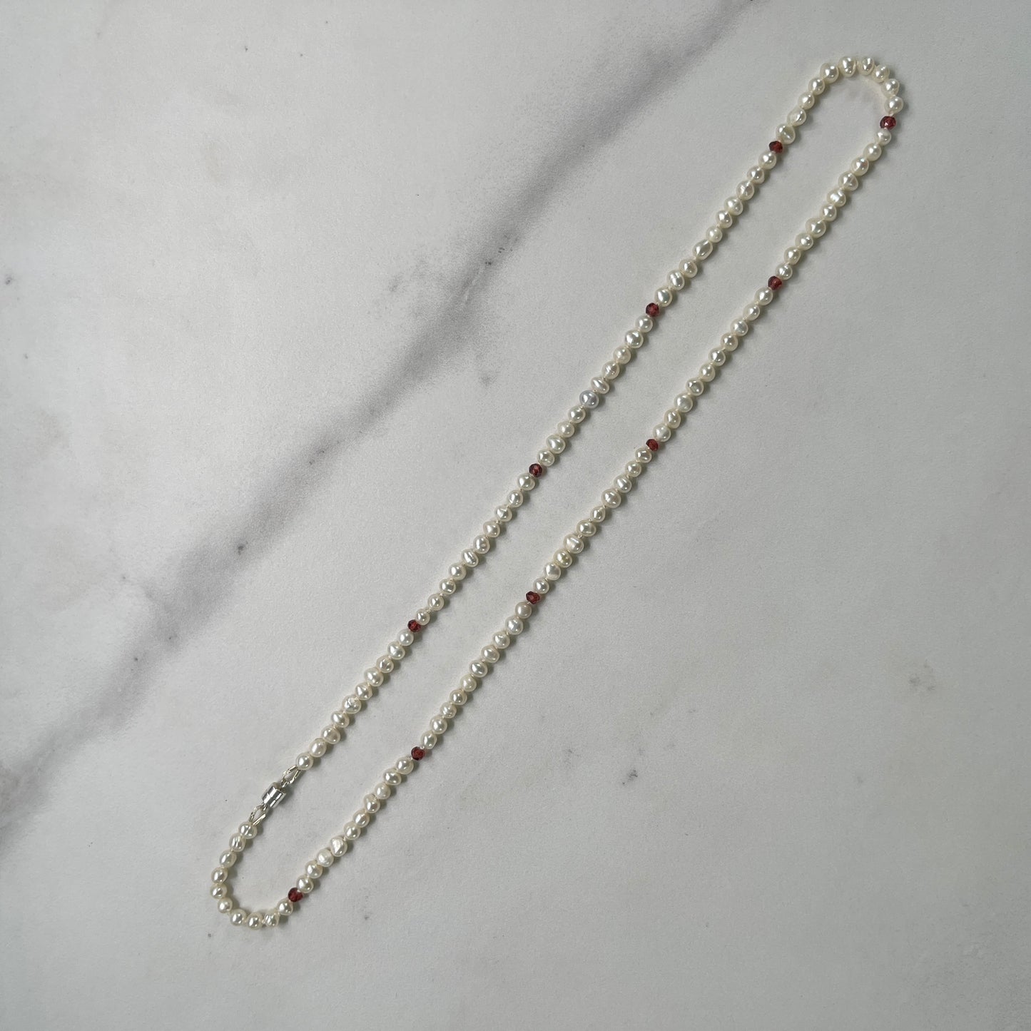 Pearl necklace with red beads on a marble surface