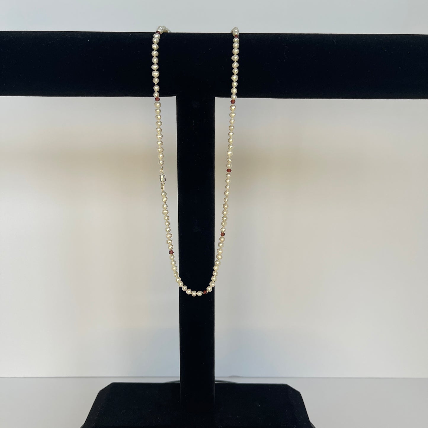 Pearl  and red cubic zirconia necklace on a black stand with a white background