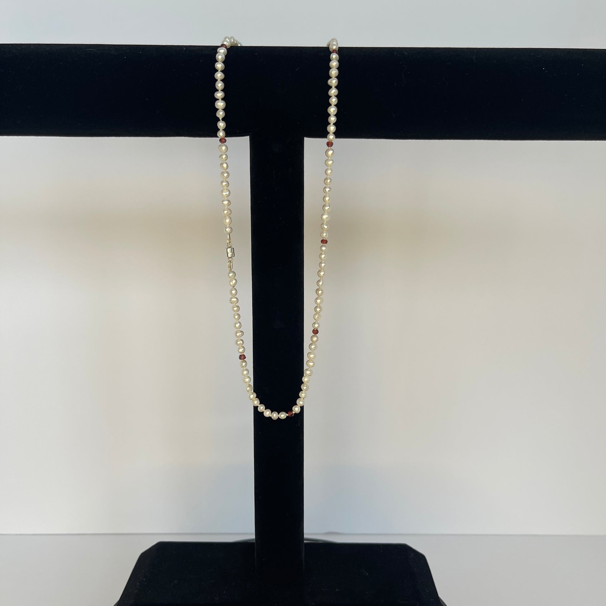 Pearl  and red cubic zirconia necklace on a black stand with a white background