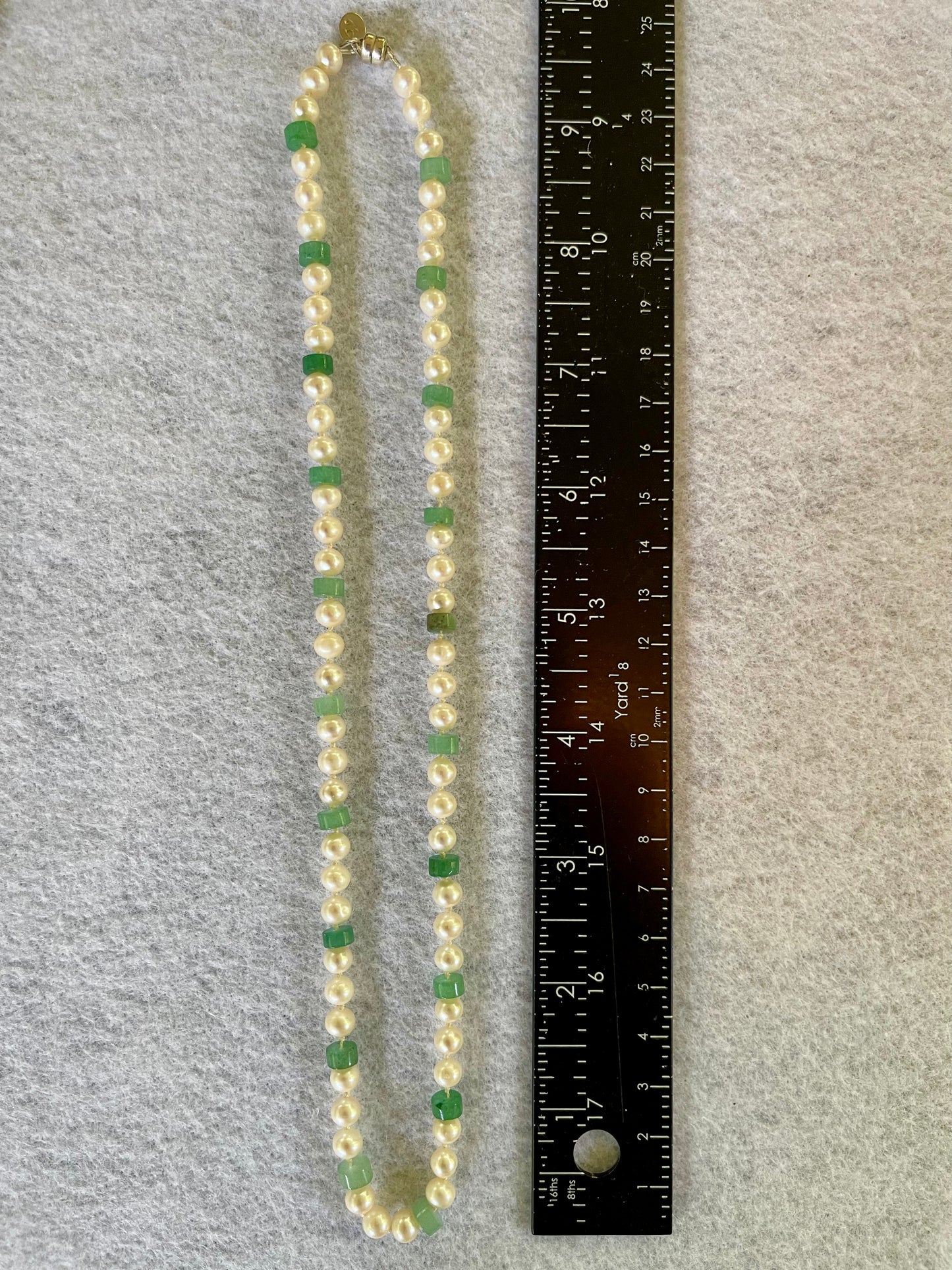 Necklace with green and white beads next to a ruler on a gray background