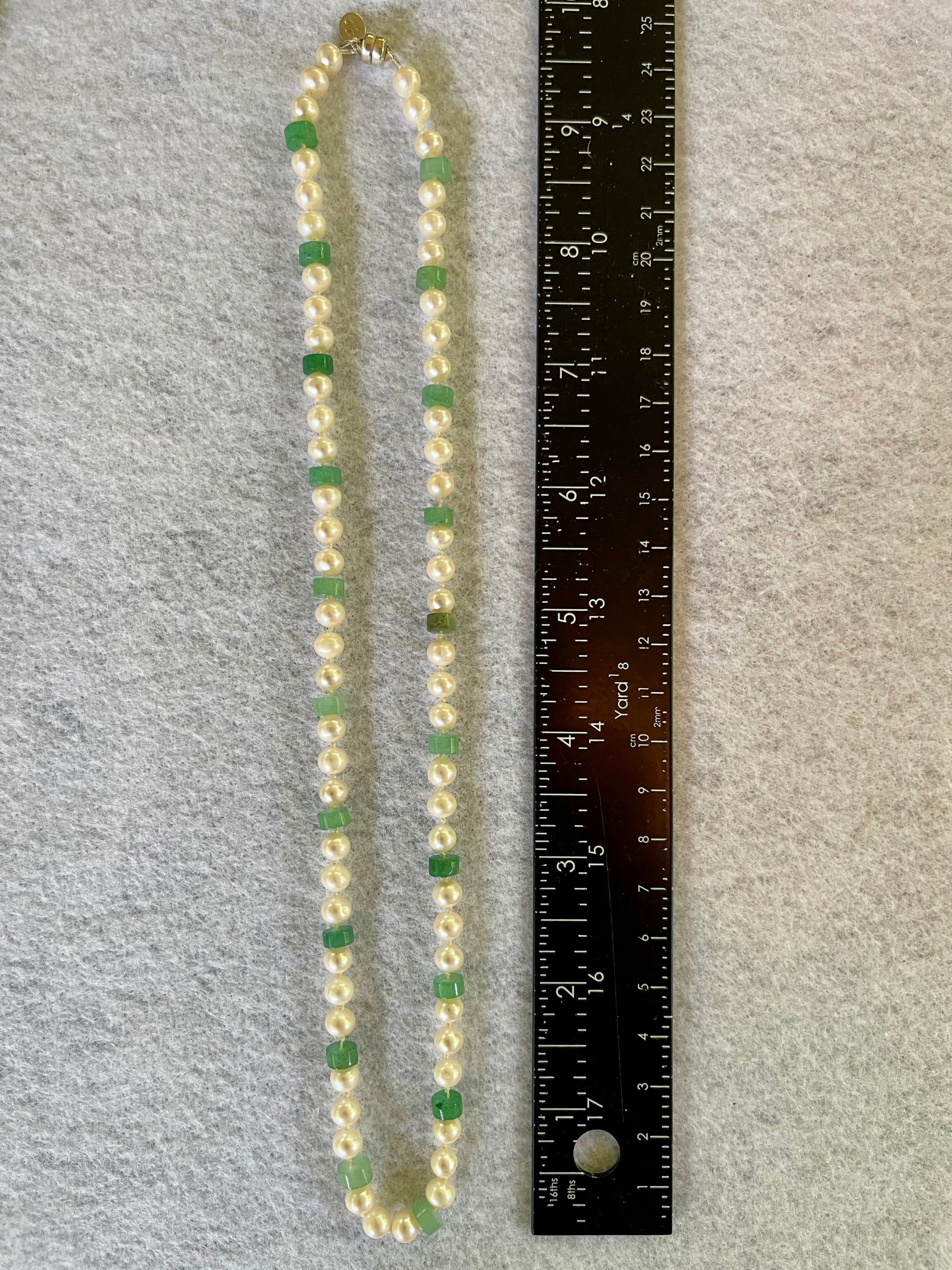 Necklace with green and white beads next to a ruler on a gray background