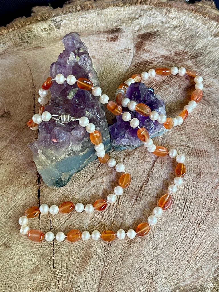 Necklace with White Pearls and oval Carnelian beads  with matching stretchy bracelet on a wooden surface with amethyst crystals.
