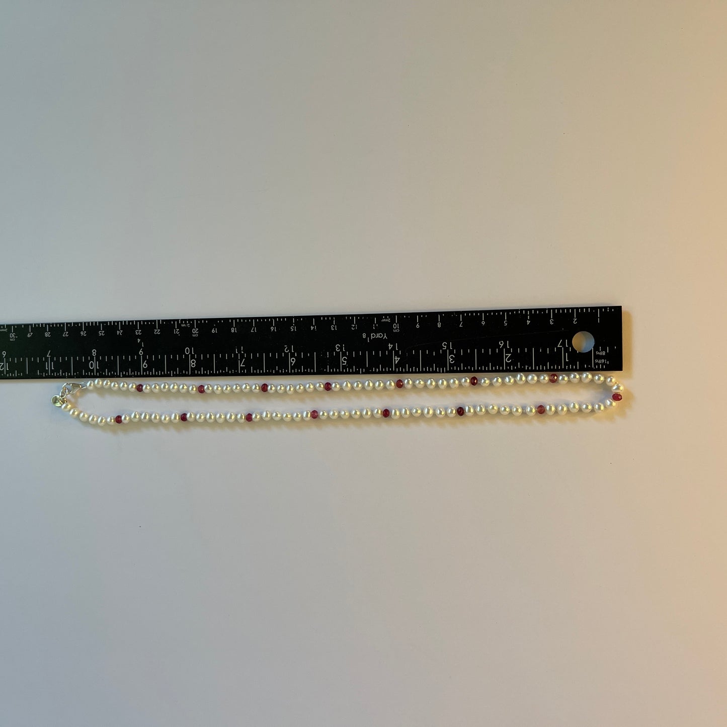 Pearl necklace laid out on a ruler for measurement against a plain background