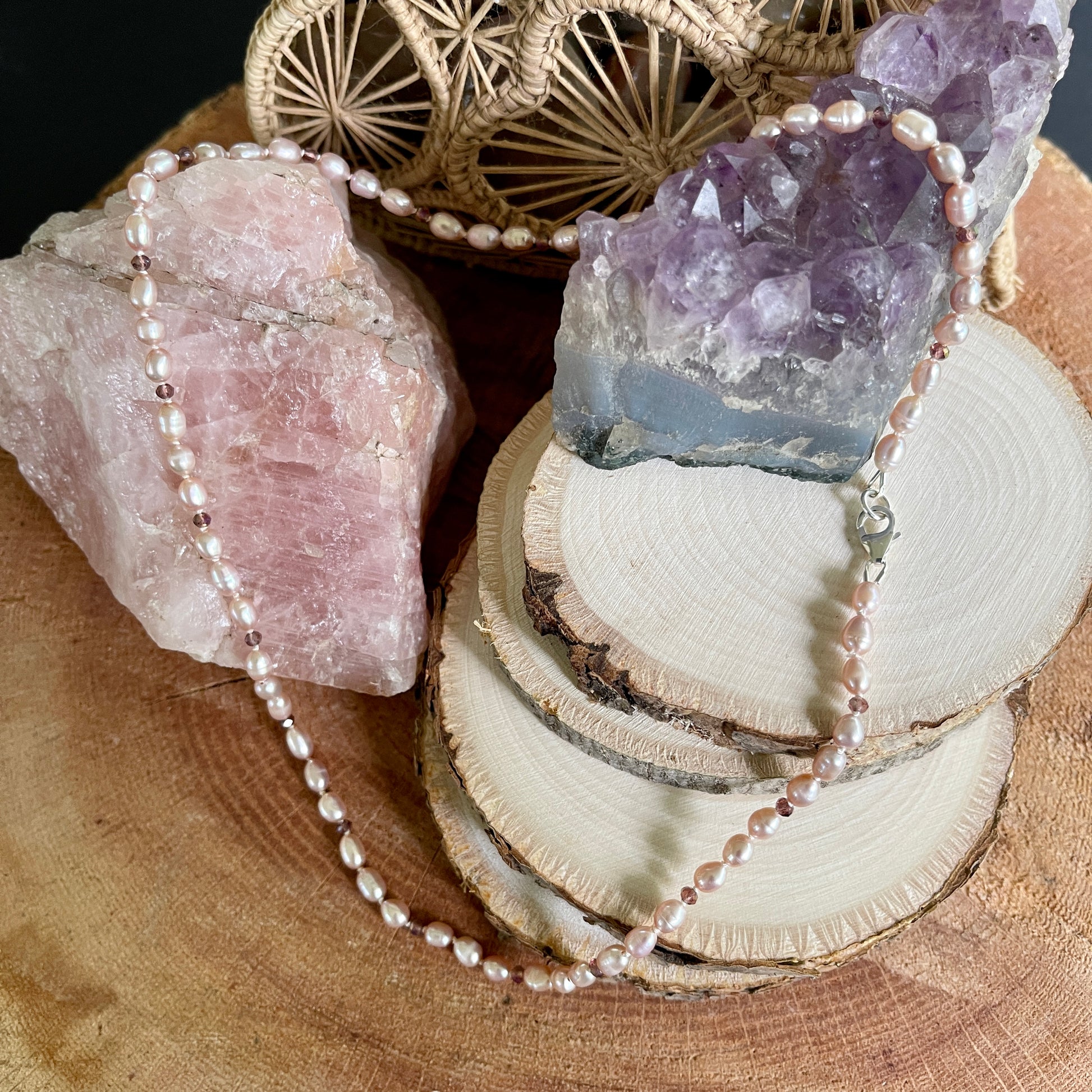 Necklace with Pink Pearls and purple cubic zirconia stones on a wooden surface with amethyst crystals and a woven decorative item.