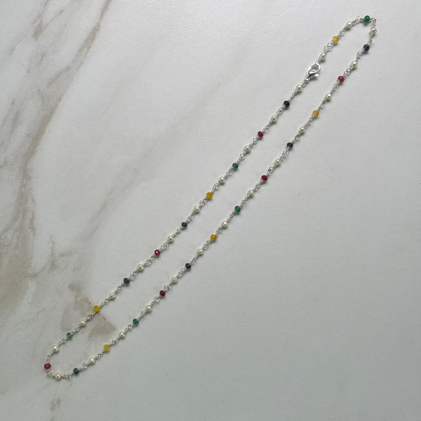 Necklace with multicolored  Jade and white Pearl beads on Sterling wire on a marble surface