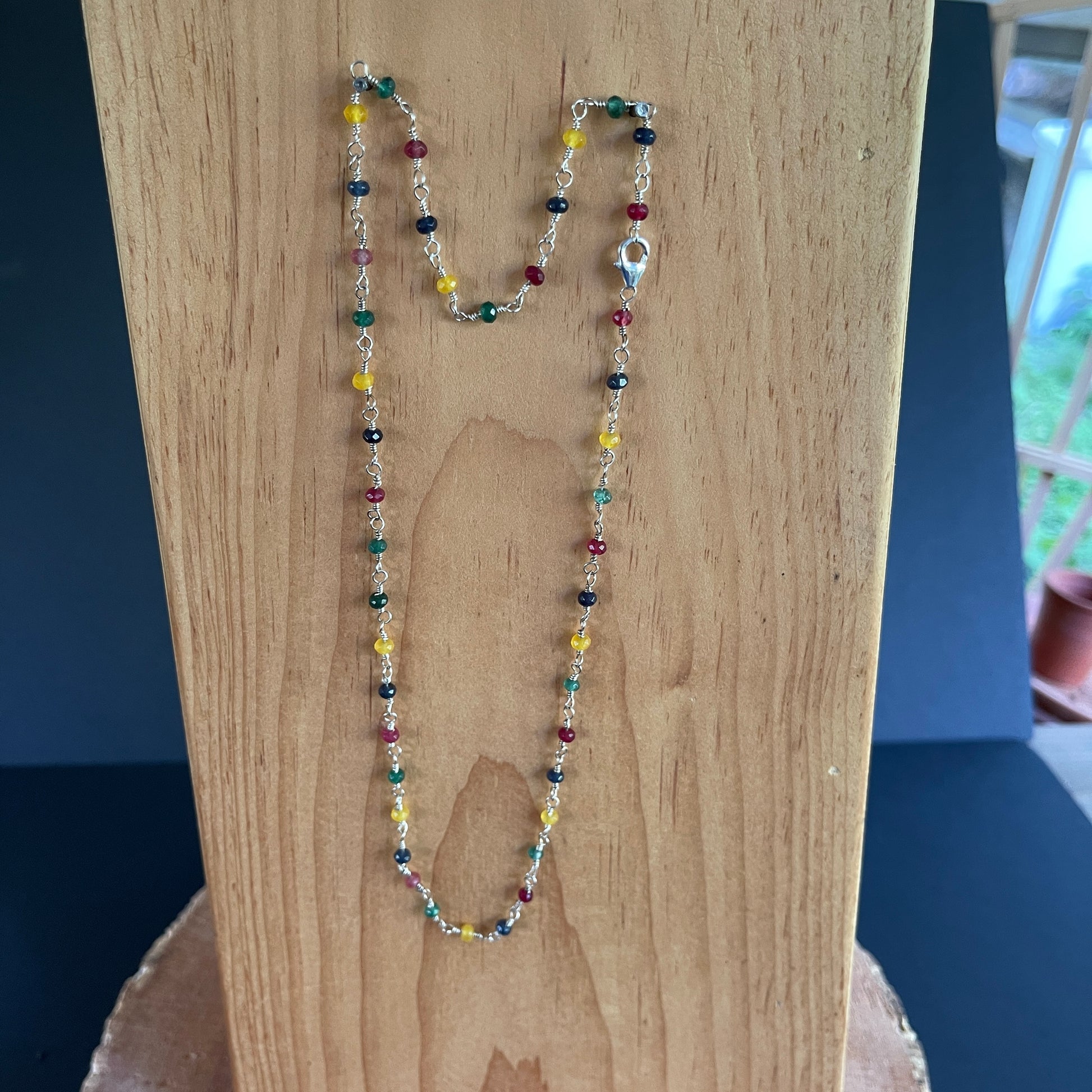 Necklace with multi colored Jade and White Pearl hand tooled on Sterling Silver wire on a wooden surface