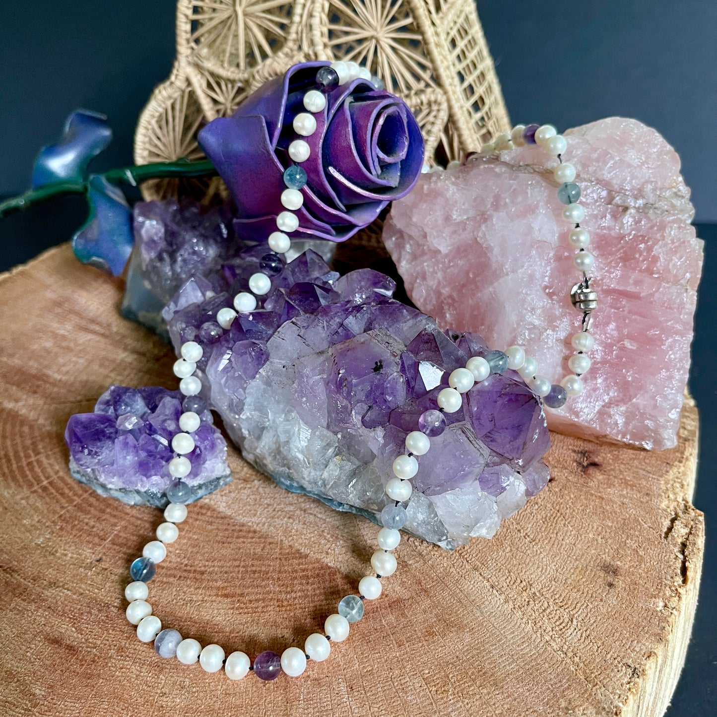 Necklace with purple rose and white Pearl and Fluorite necklace on a wooden surface with crystals