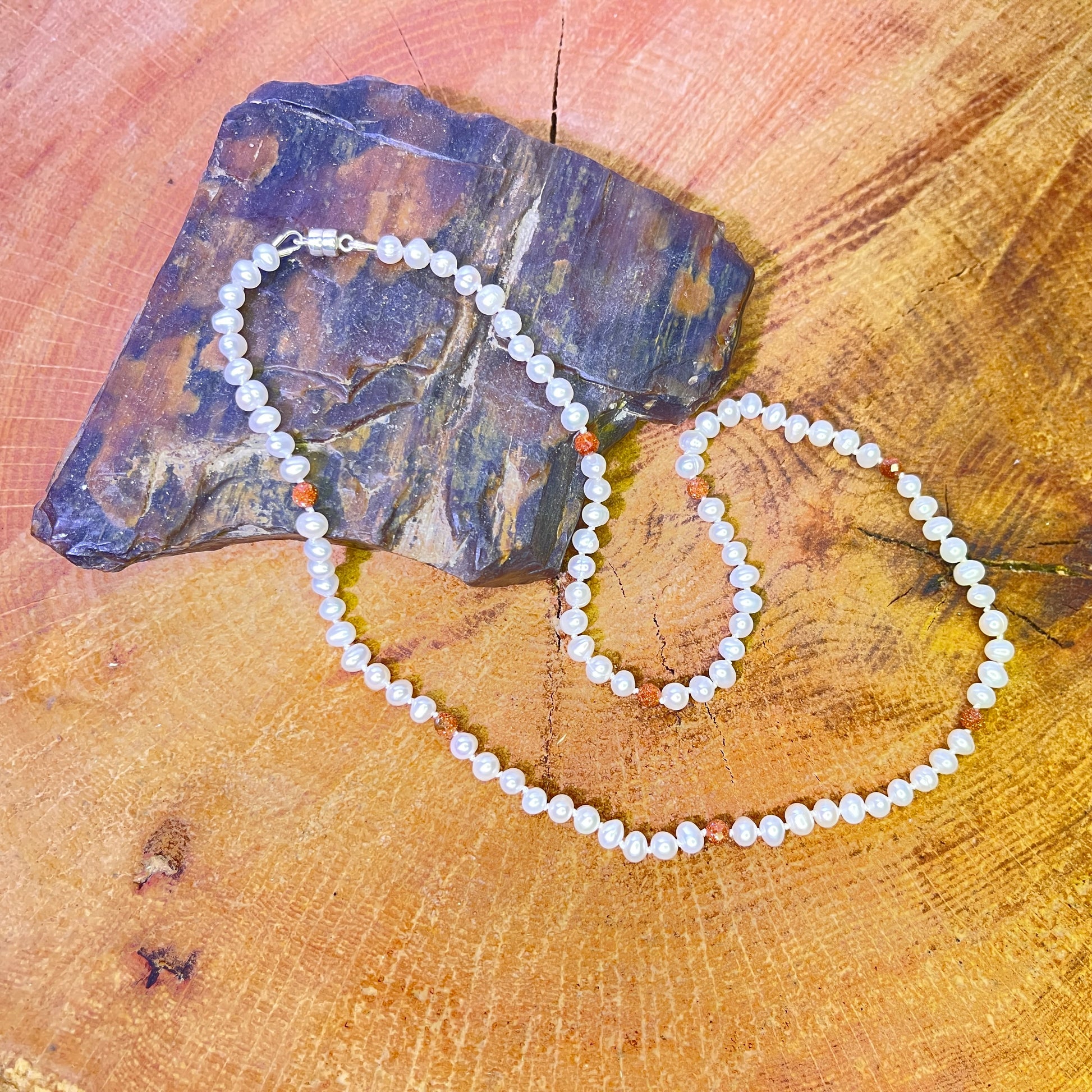 Pearl  and goldstone necklace on a wooden surface with a stone
