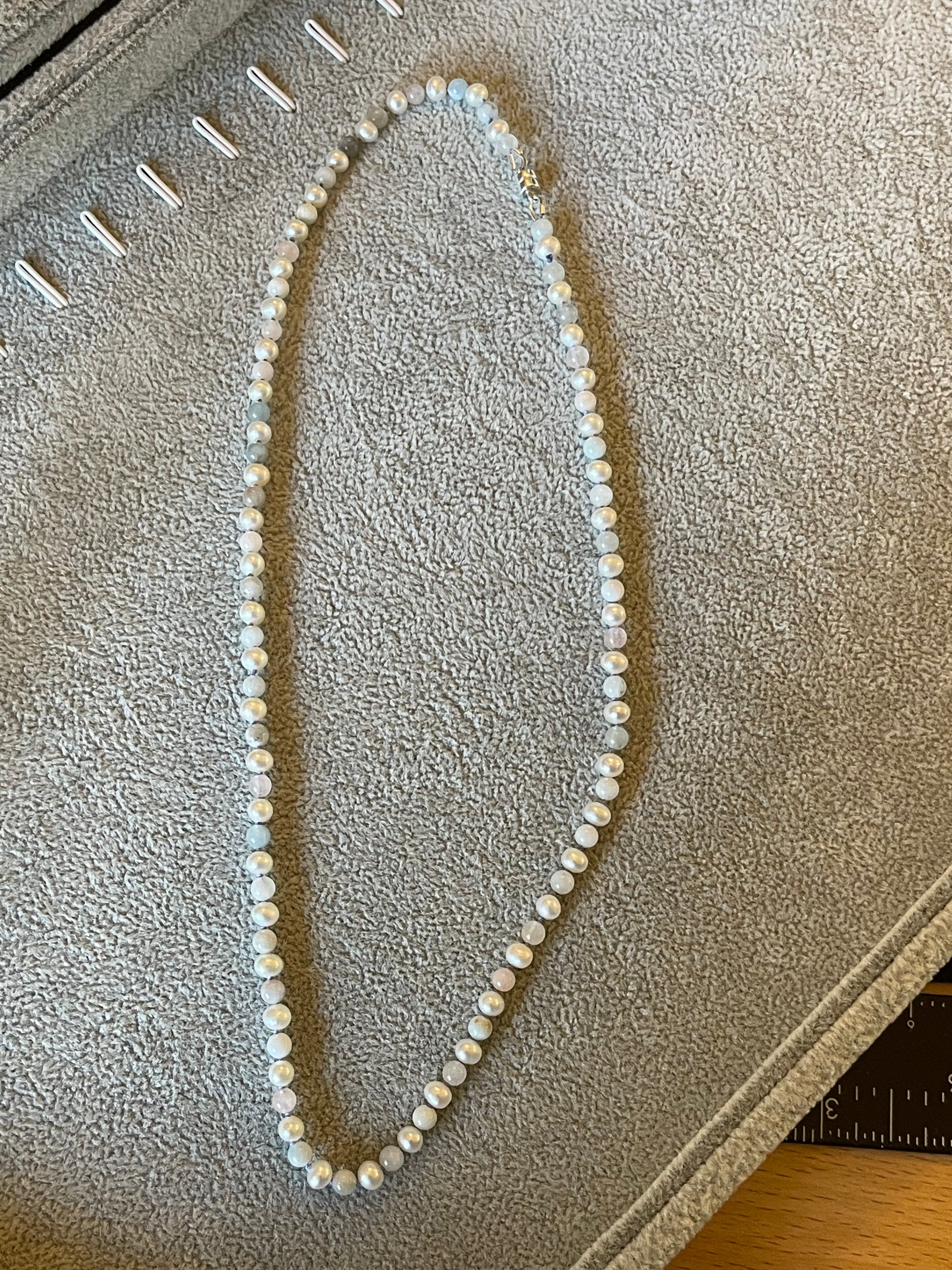 Pearl necklace on a textured surface with a ruler for scale