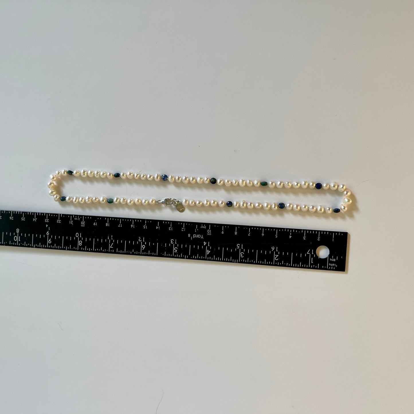 Pearl necklace with blue jasper beads on a gray background, measured by a ruler.