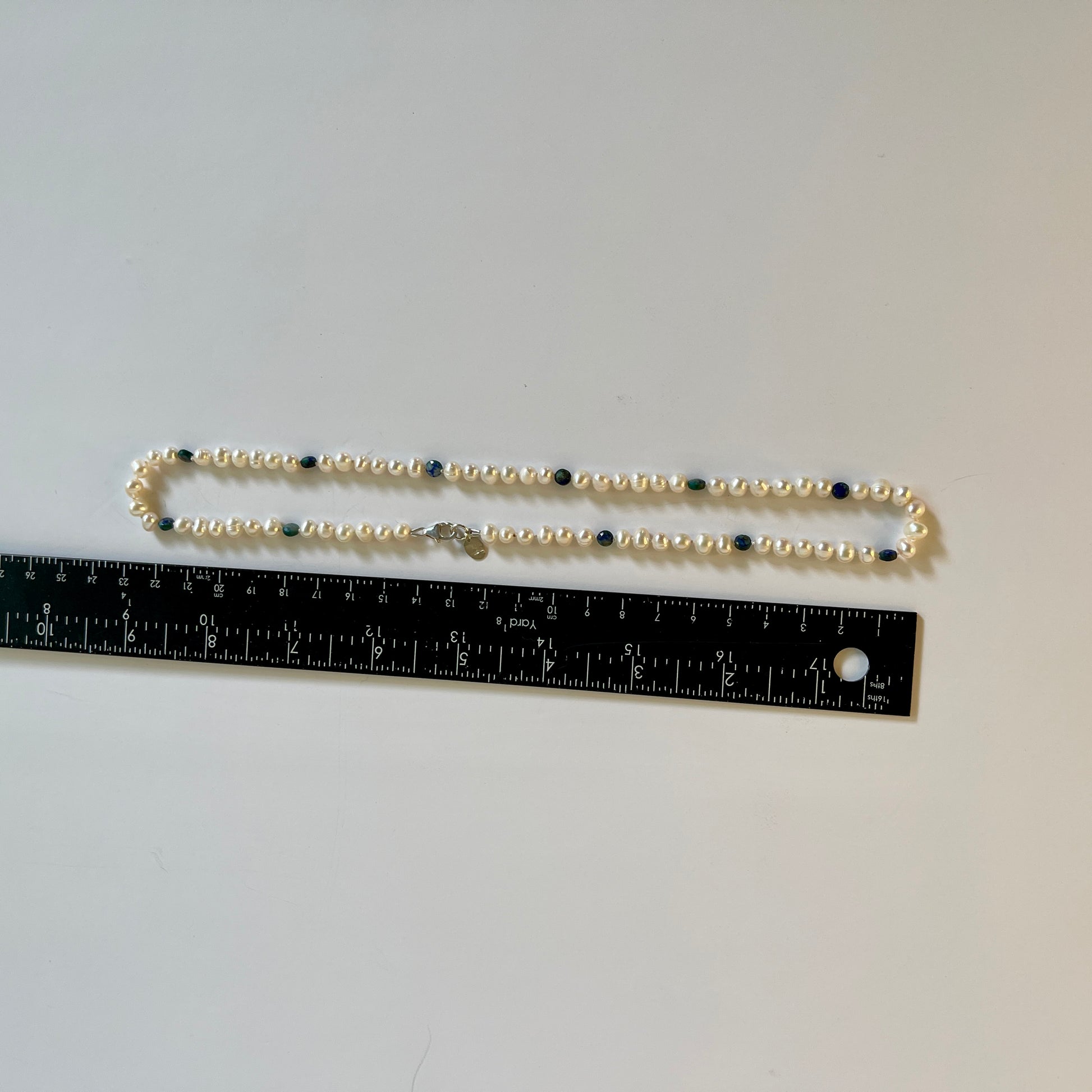 Pearl necklace with blue jasper beads on a gray background, measured by a ruler.
