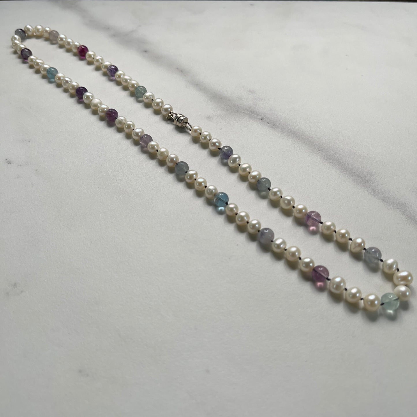 Necklace with pearls and multicolored Fluorite beads on a light gray marble background