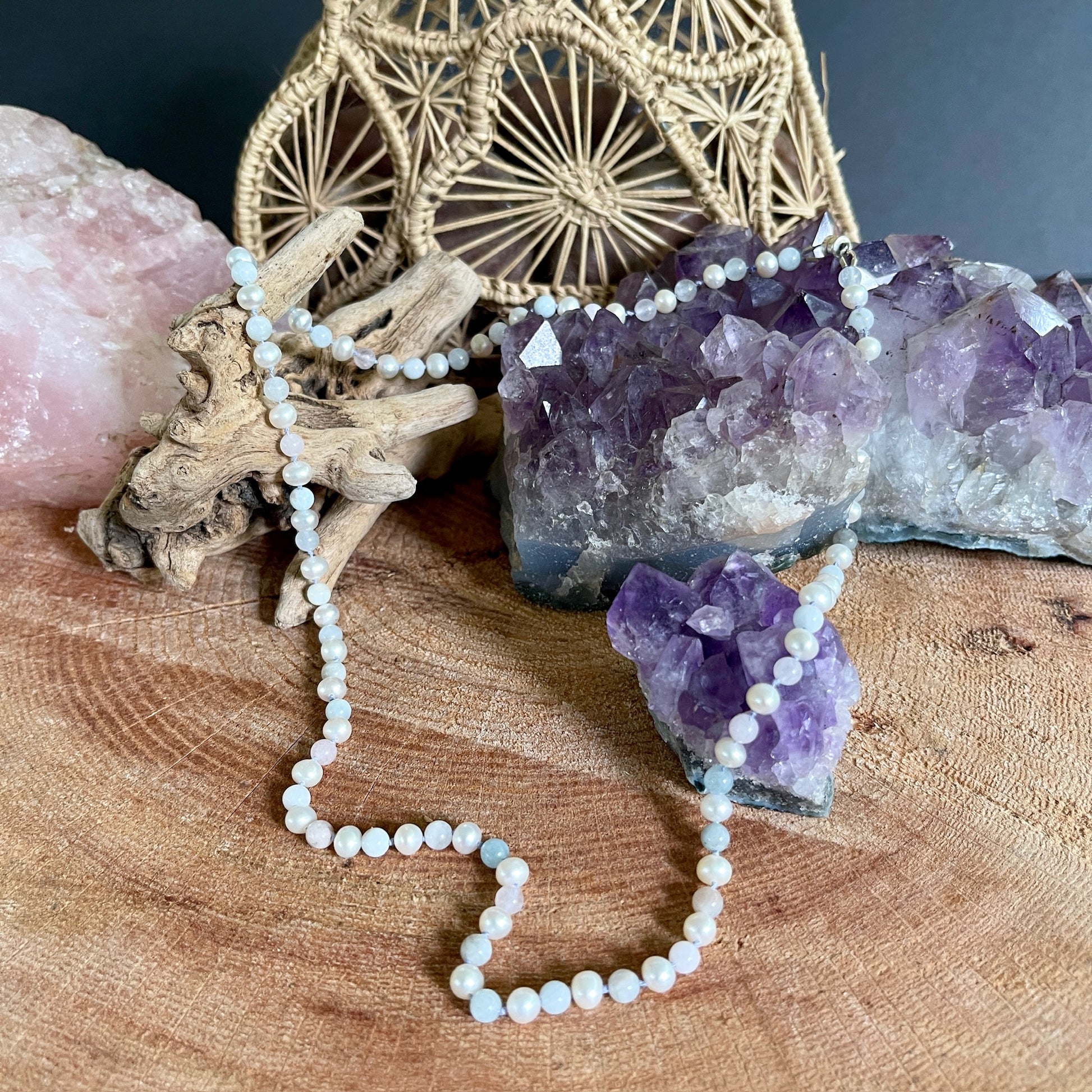 Pearl and morganite necklace on a wooden surface with amethyst crystals and a woven basket in the background.